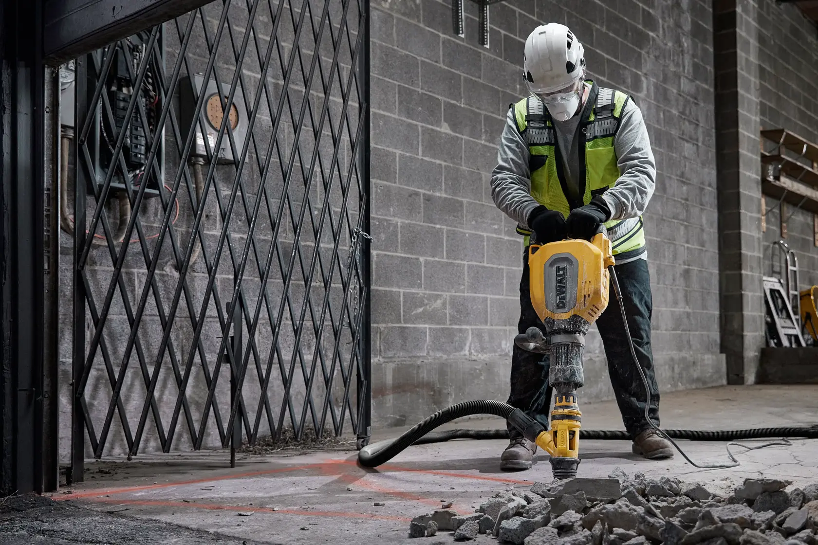 Worker breaks concrete floor with DEWALT jackhammer D25911K in industrial setting, rubble scattered on ground.