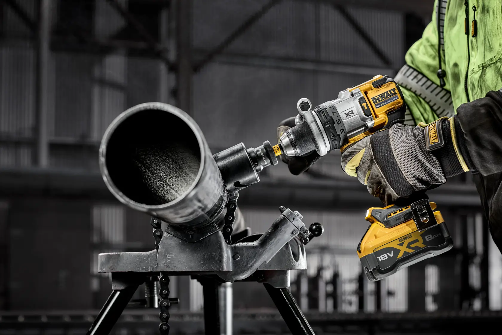 Worker uses DEWALT XR 18V power tool with battery to drill into a metal pipe in an industrial setting.