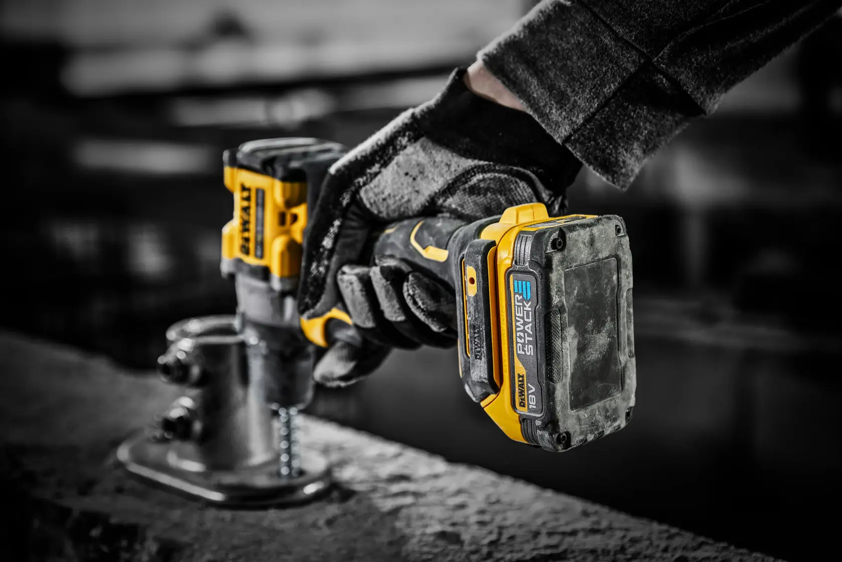 DEWALT Powerstack 18V battery attached to a cordless drill, used by a gloved hand on a construction site.