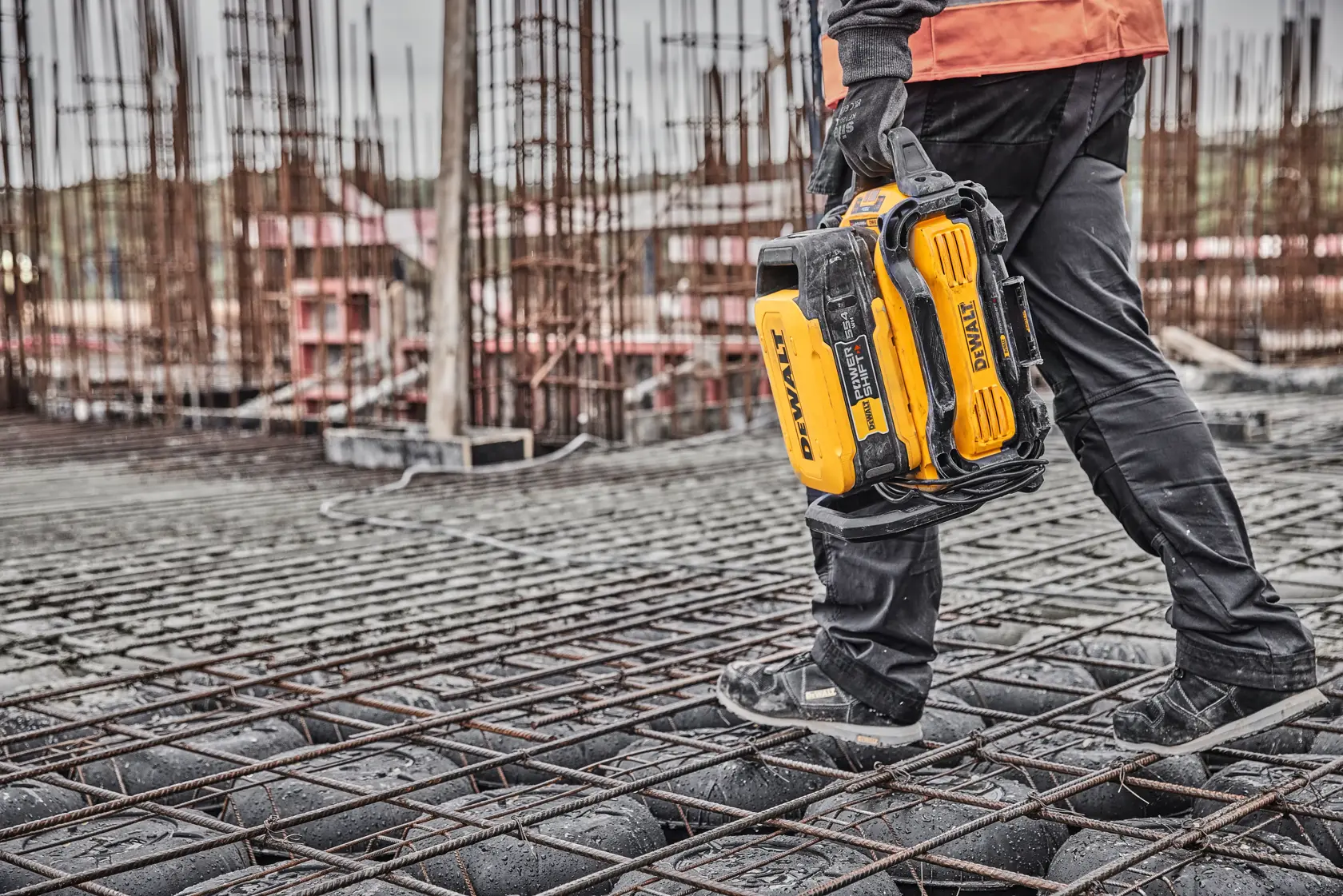 Person walking on construction site holding a DEWALT tool case.