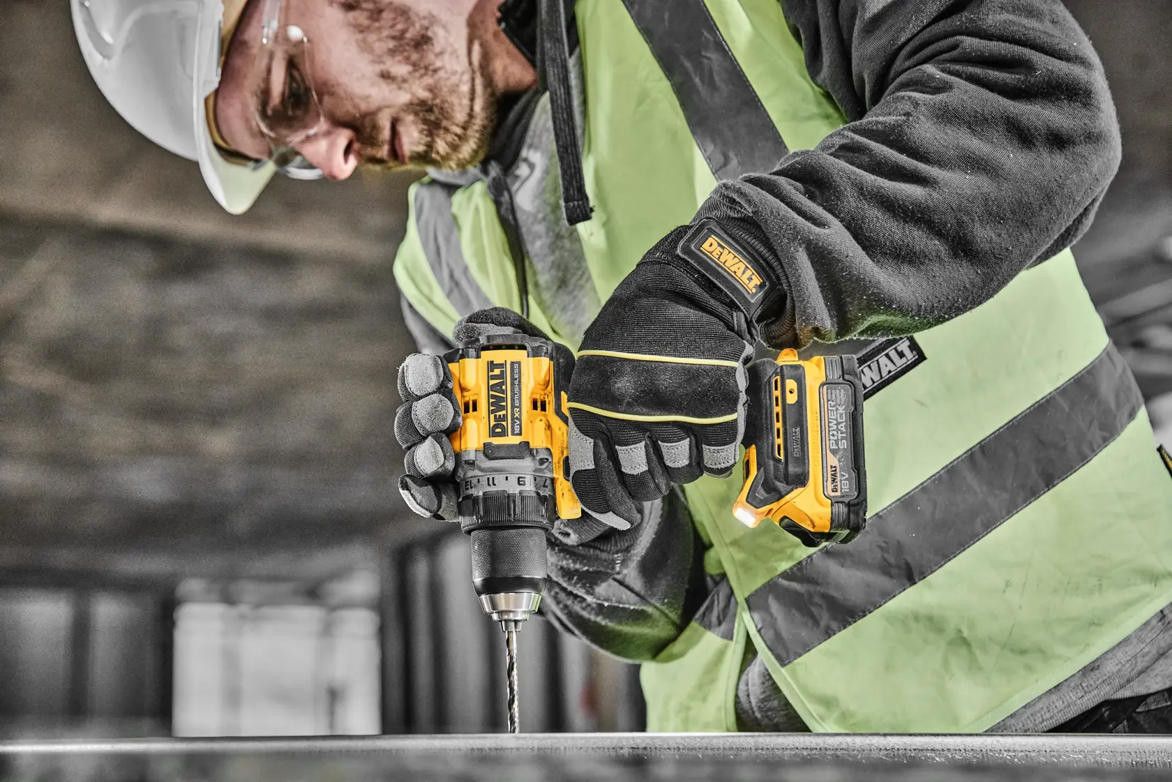A construction worker wearing safety gear uses a yellow DEWALT cordless drill to drill into metal.