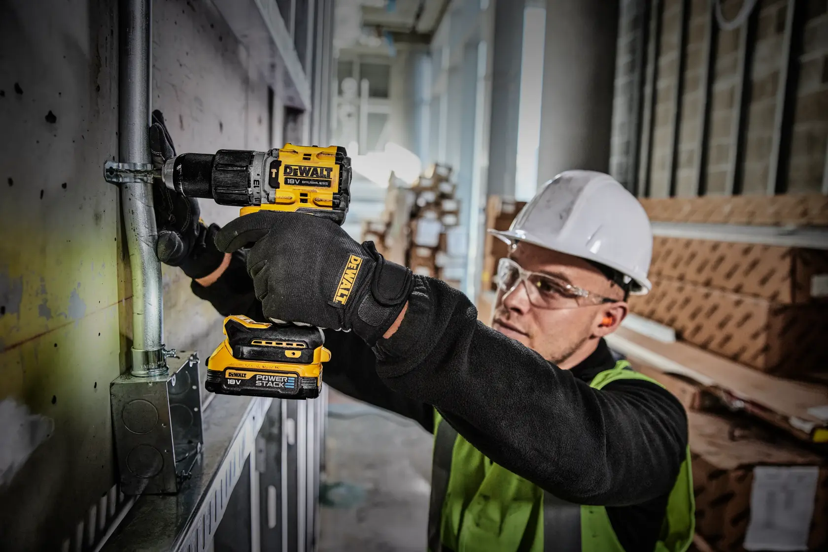 Worker uses a DEWALT DCD805E2T drill on a metal pipe in a construction site while wearing safety gear.
