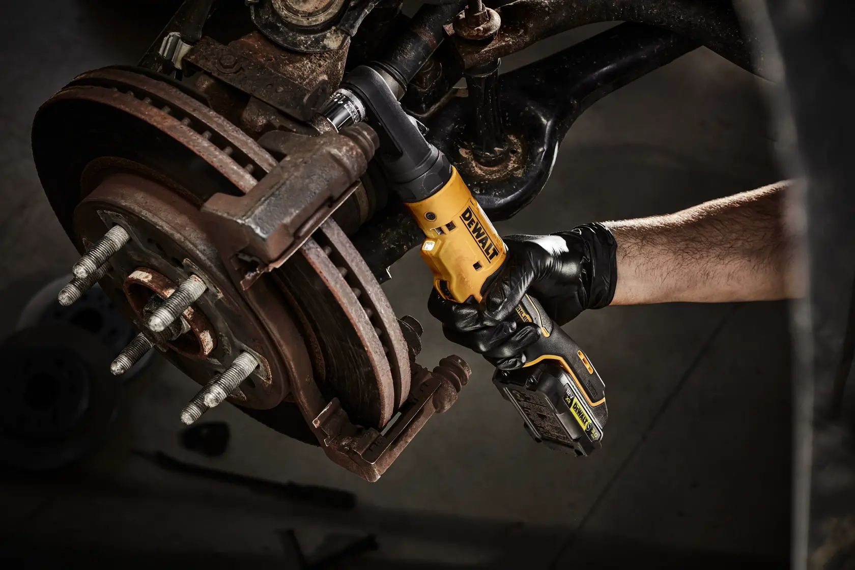 Person uses DEWALT cordless ratchet tool on vehicle brake assembly.