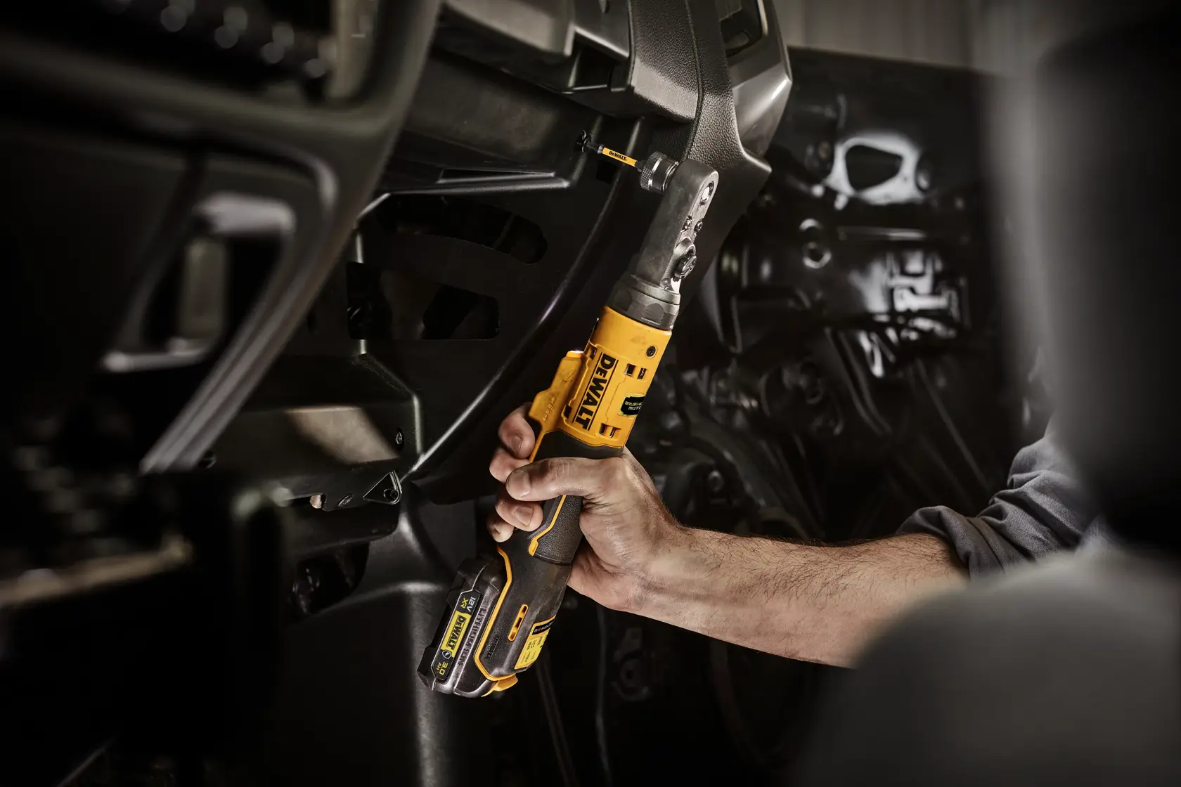 Hand uses a yellow DEWALT cordless ratchet tool inside a vehicle for mechanical work.