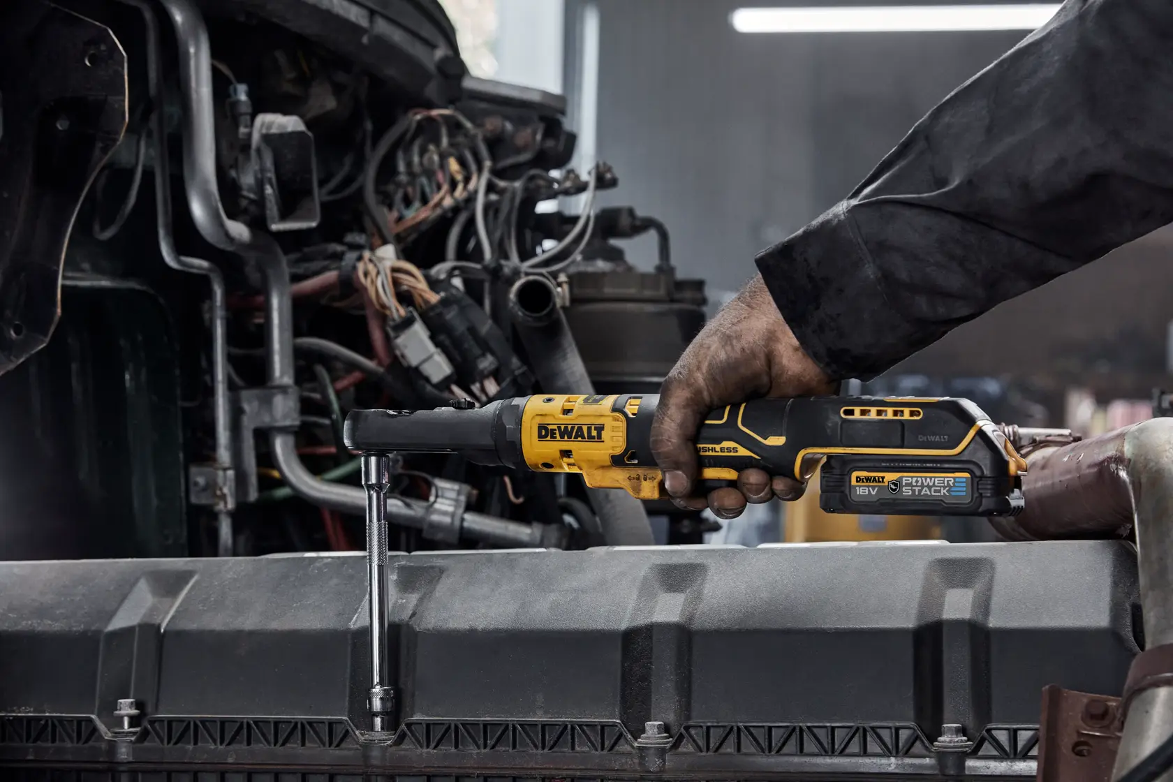 Person using a DEWALT cordless ratchet tool to work on machinery in an industrial setting.