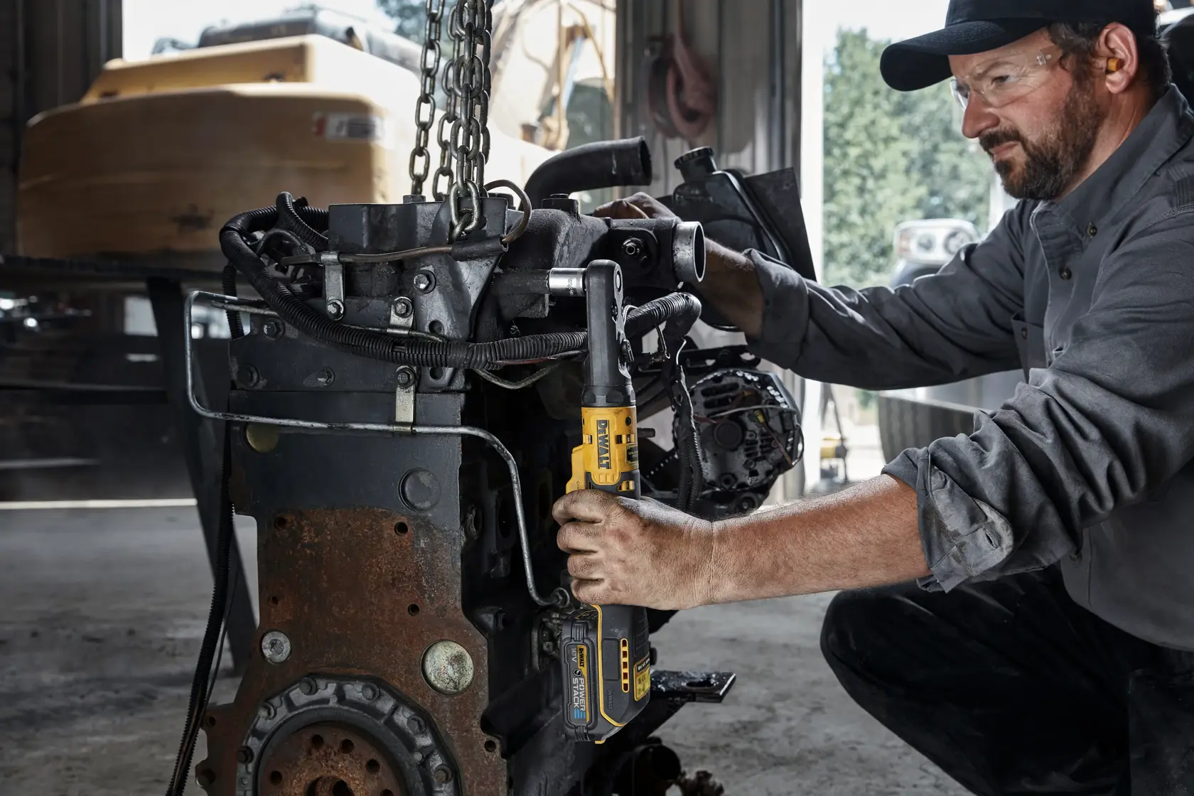 Person uses a DEWALT cordless ratchet tool on machinery in an industrial workshop setting.