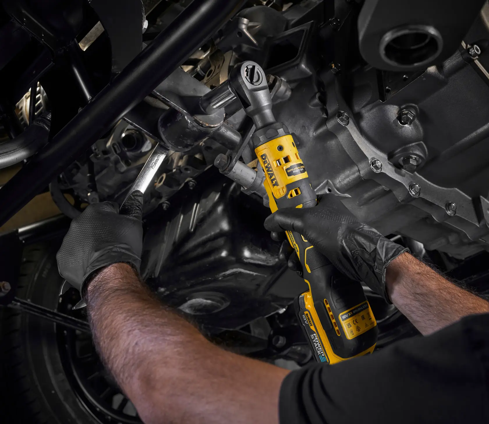 Person uses a DEWALT cordless ratchet tool DCF512N on an engine while wearing gloves.