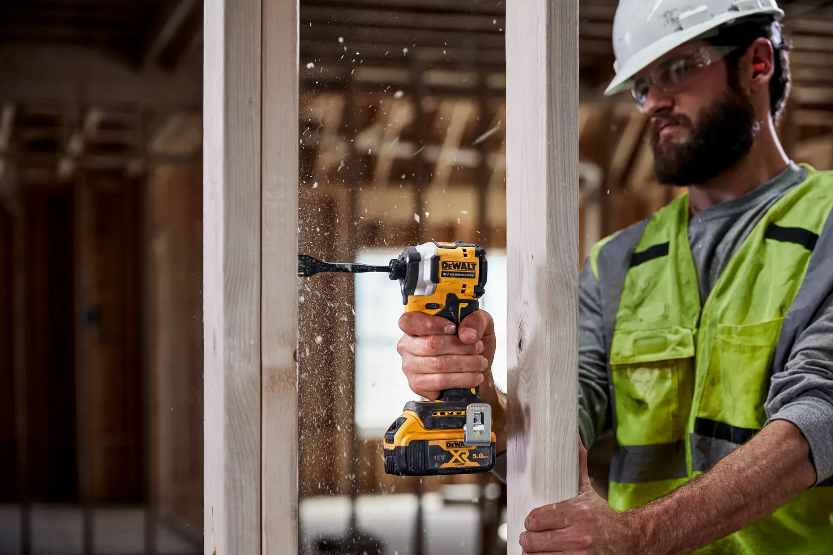 Person uses DEWALT cordless drill to bore a hole in a wooden beam at a construction site.