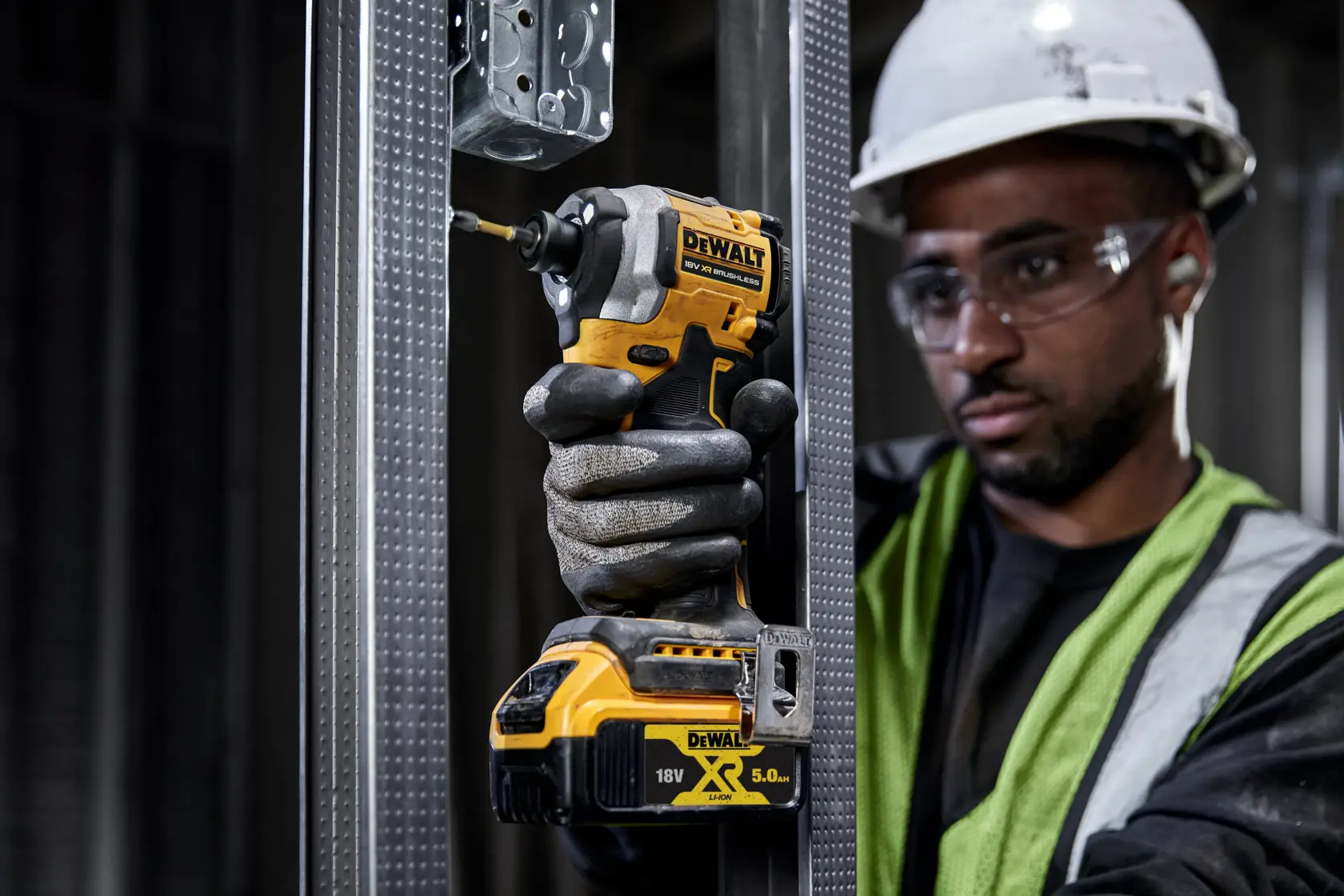Worker uses a DEWALT DCF850P2T cordless impact driver on a metal frame at a construction site.