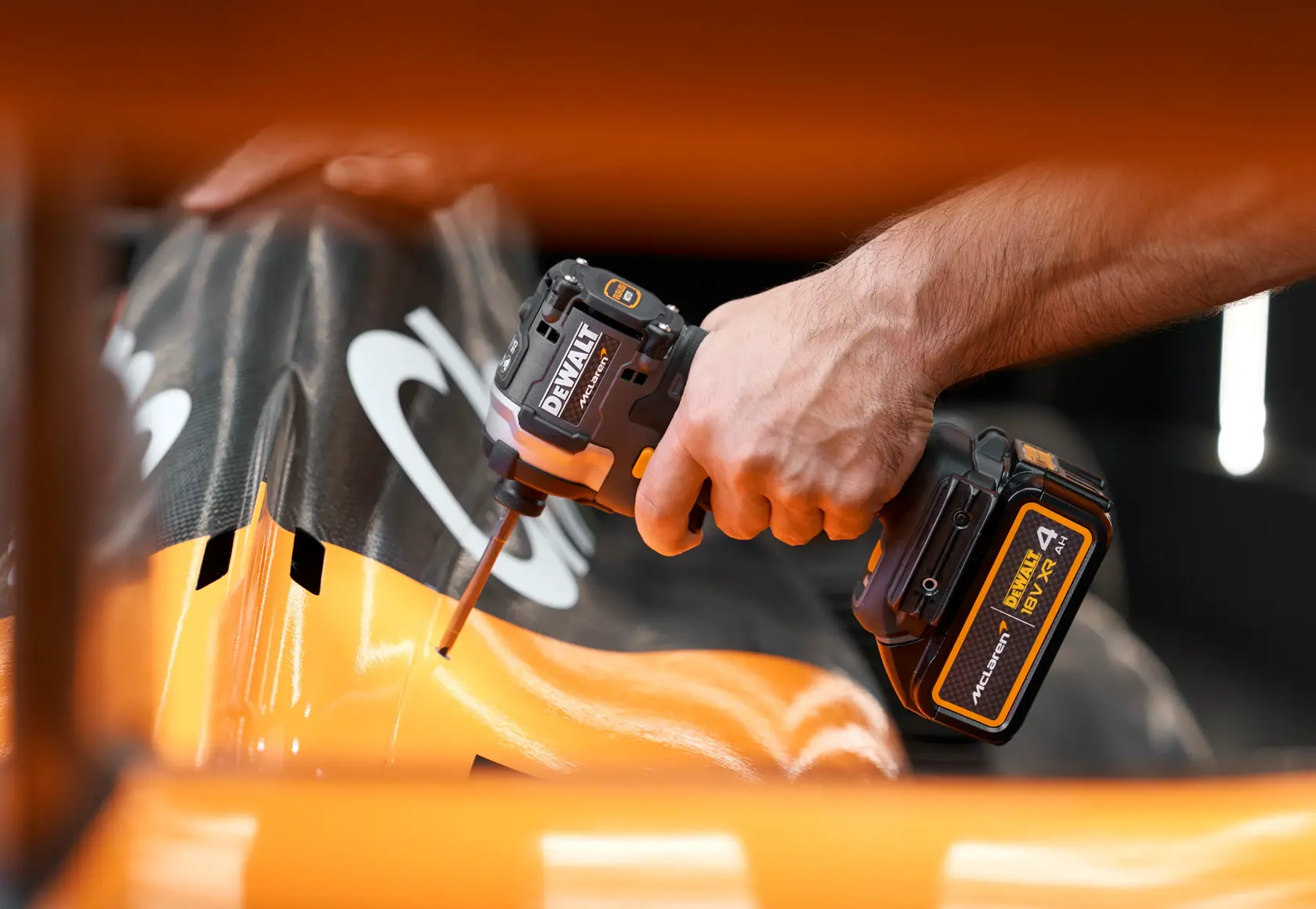 A DEWALT cordless impact driver is used on an orange and black surface, close-up of hand and tool in action.