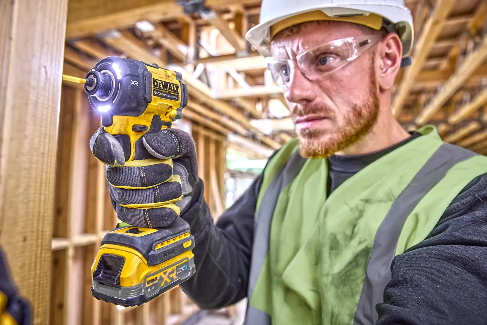 Person using a DEWALT DCF870 cordless impact wrench at a construction site, wearing gloves and a safety vest.