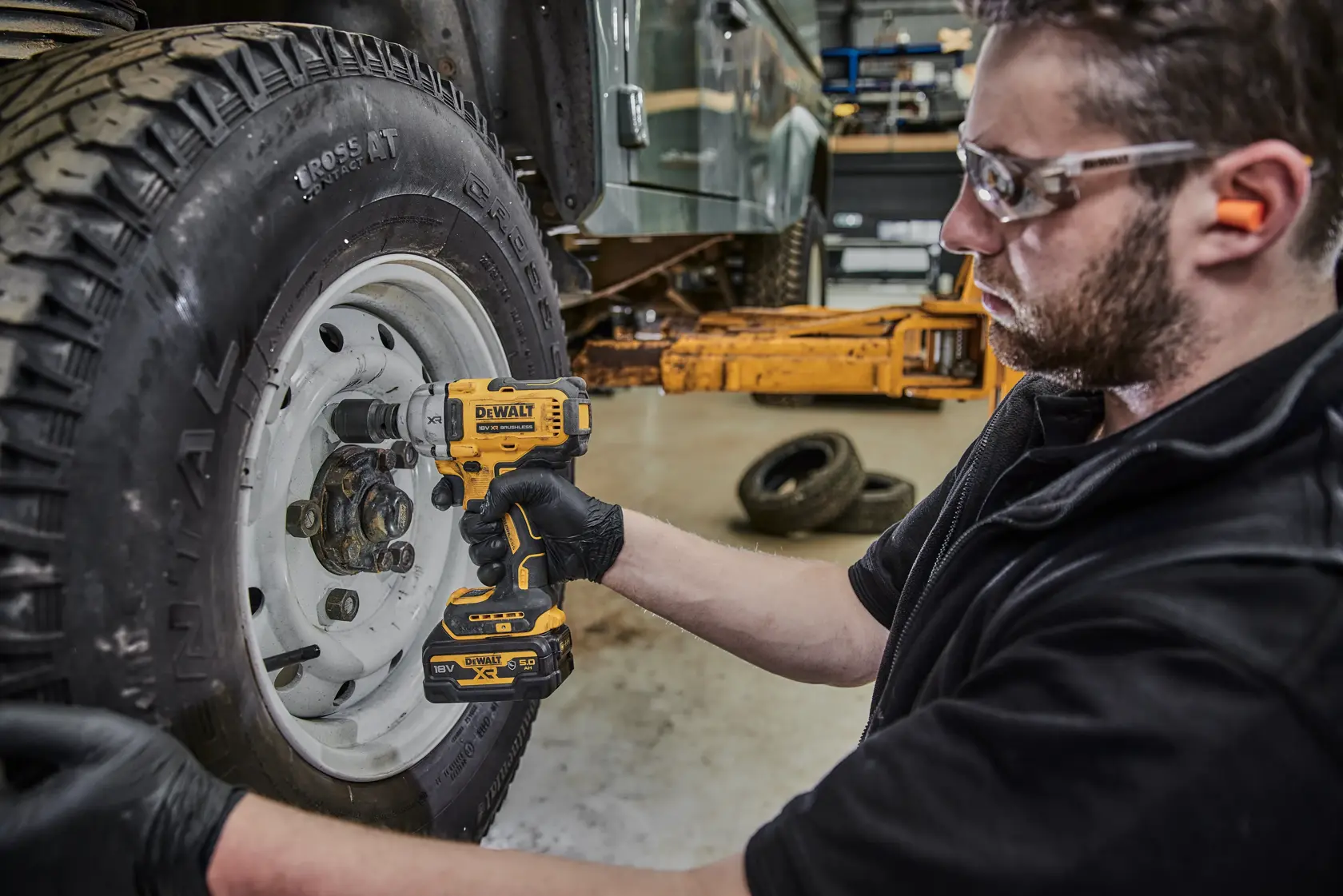 Person uses DEWALT cordless impact wrench to work on car wheel in a workshop.