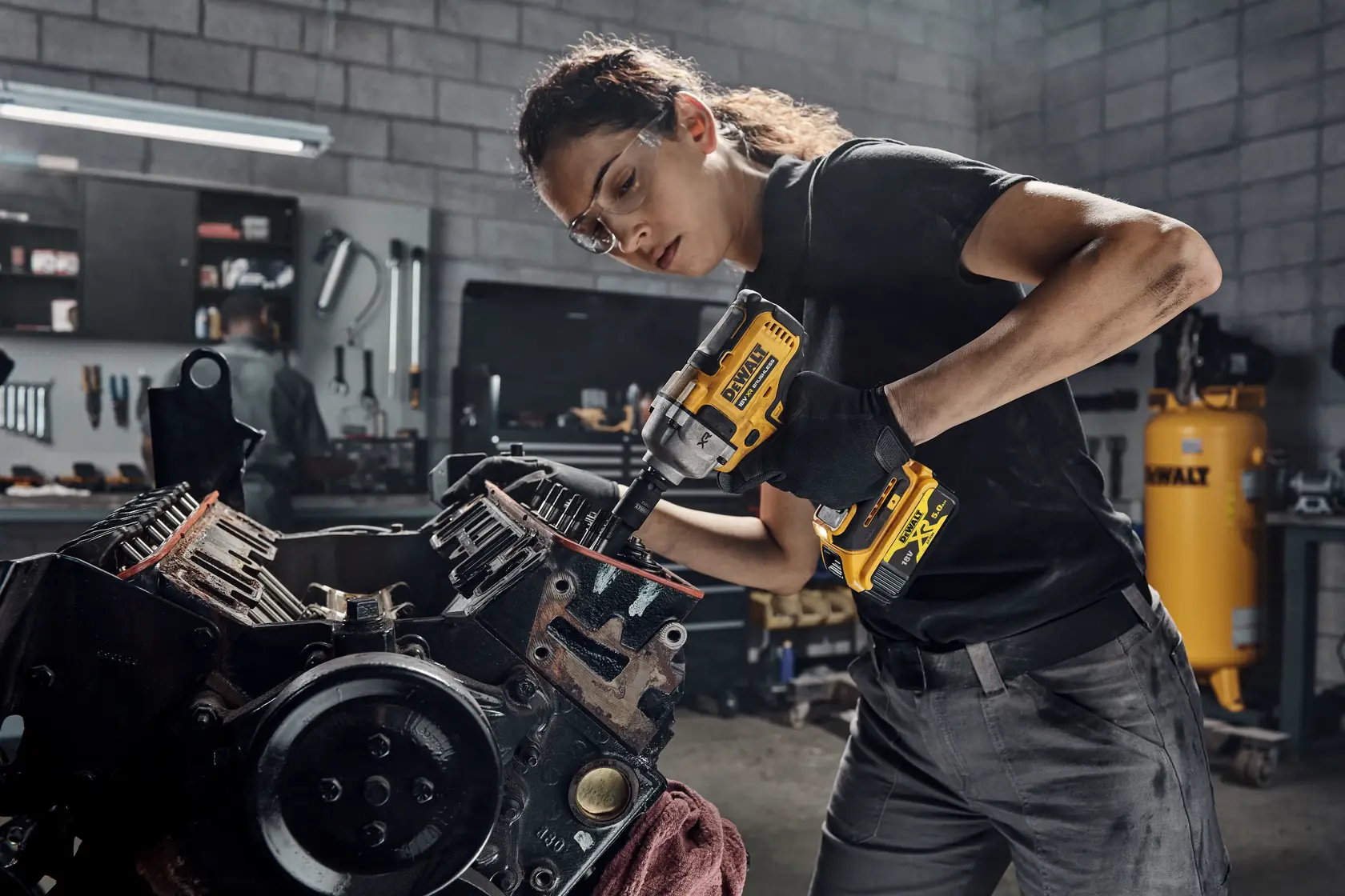 Person using a DEWALT DCF892NT impact wrench on machinery in a workshop.