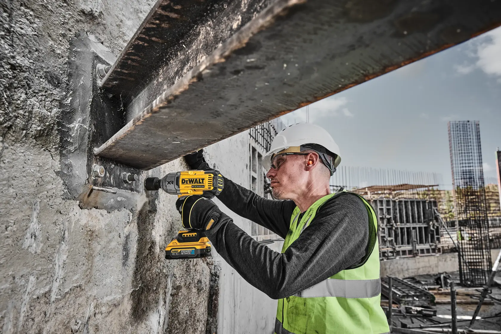 Worker using a DEWALT DCF900H2T drill on a steel beam at a construction site, wearing safety gear and helmet.
