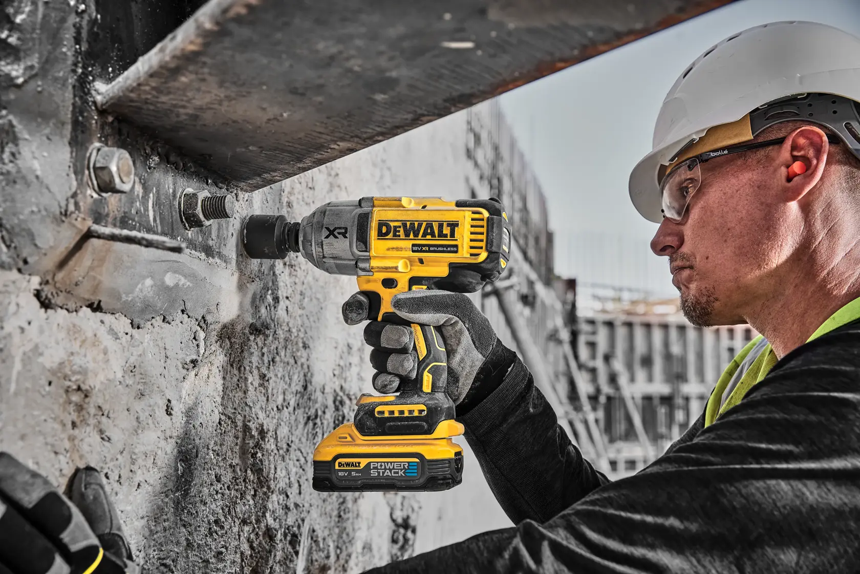 Worker uses DEWALT cordless impact wrench on a concrete structure at a construction site.
