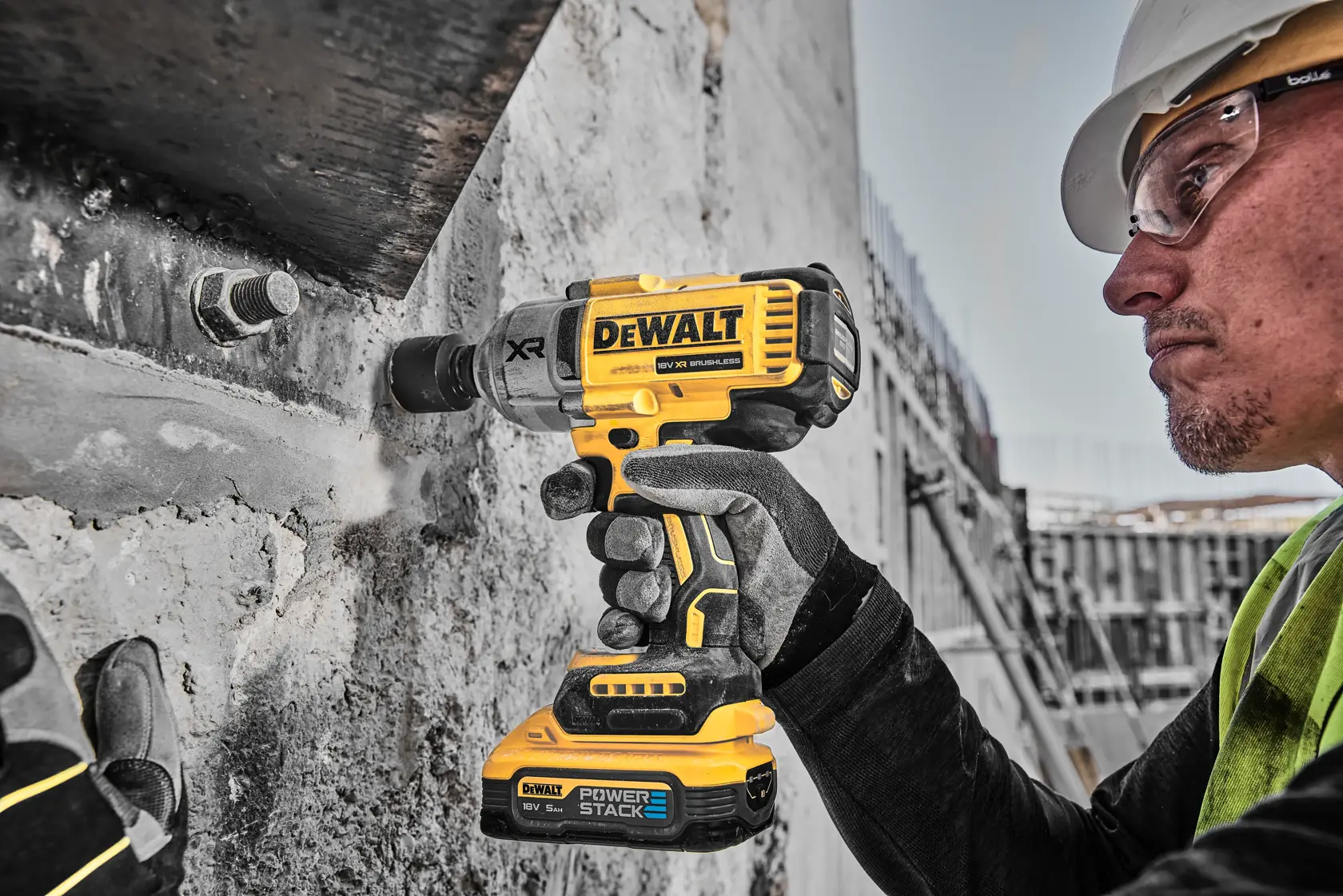 Worker using yellow DEWALT DCF900H2T impact wrench on concrete with gloves at construction site.