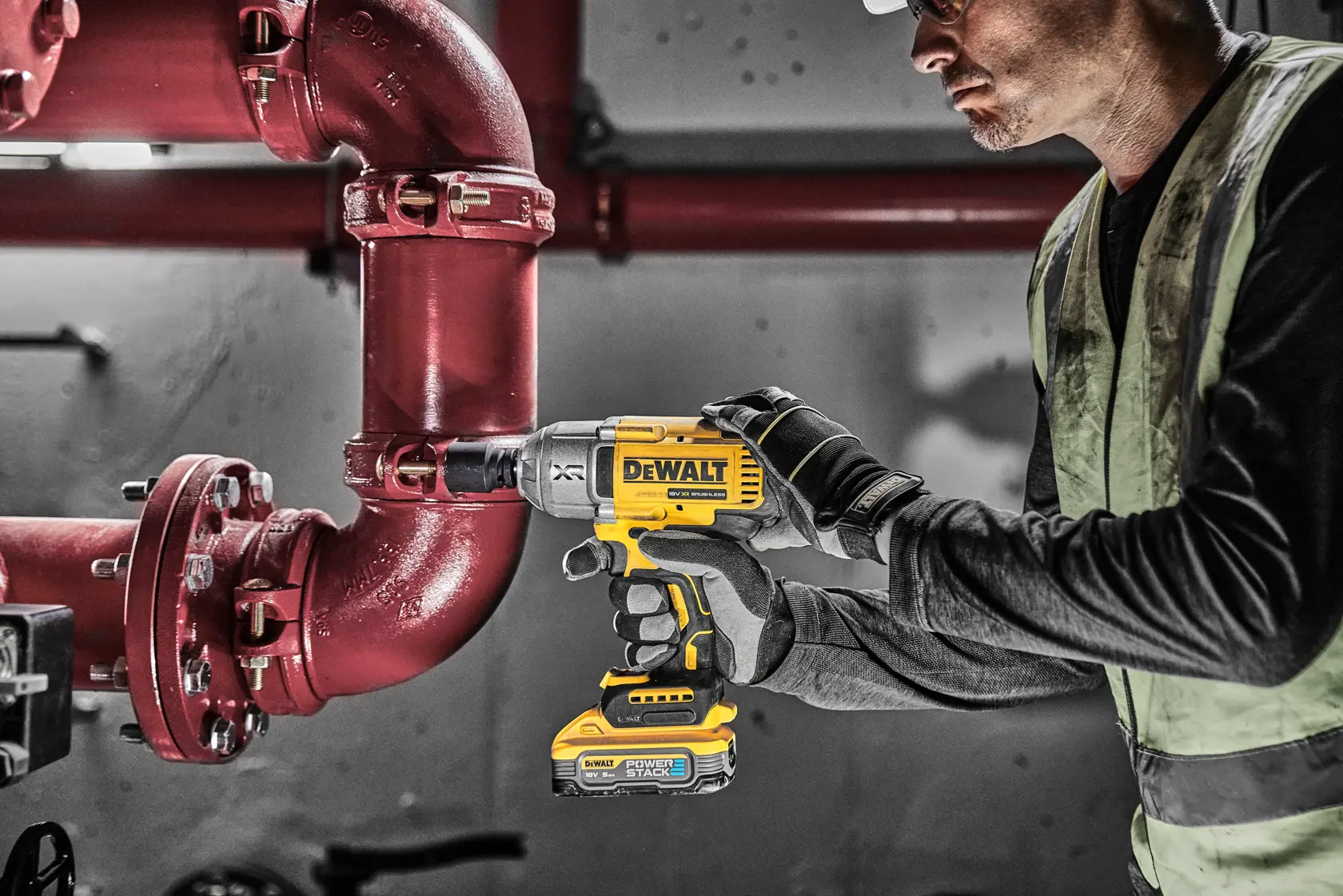 Person uses DEWALT DCF900H2T impact wrench on a red pipe in an industrial setting.