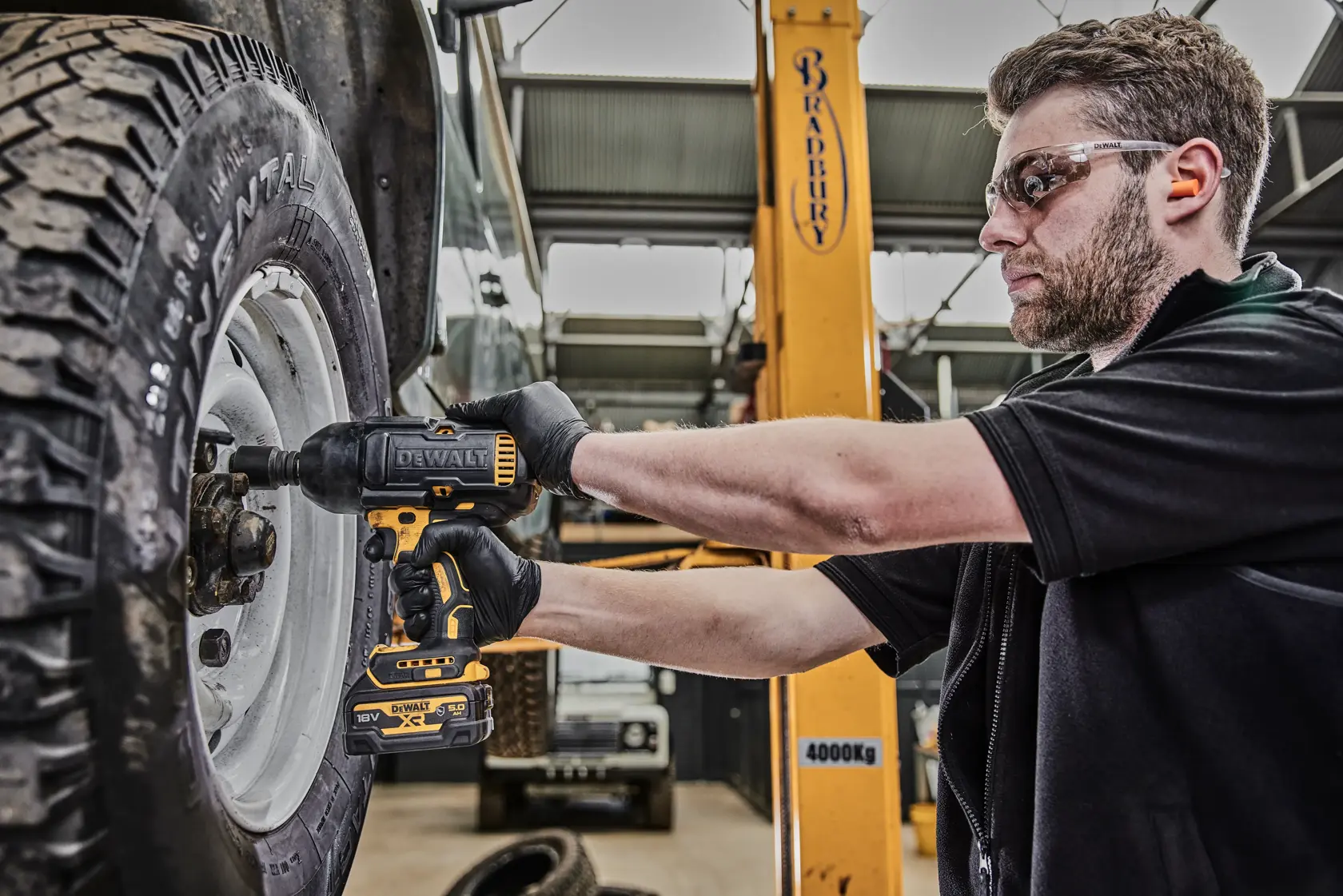 Person using a DEWALT DCF900P2G impact wrench to tighten wheel nuts on a vehicle inside a workshop.