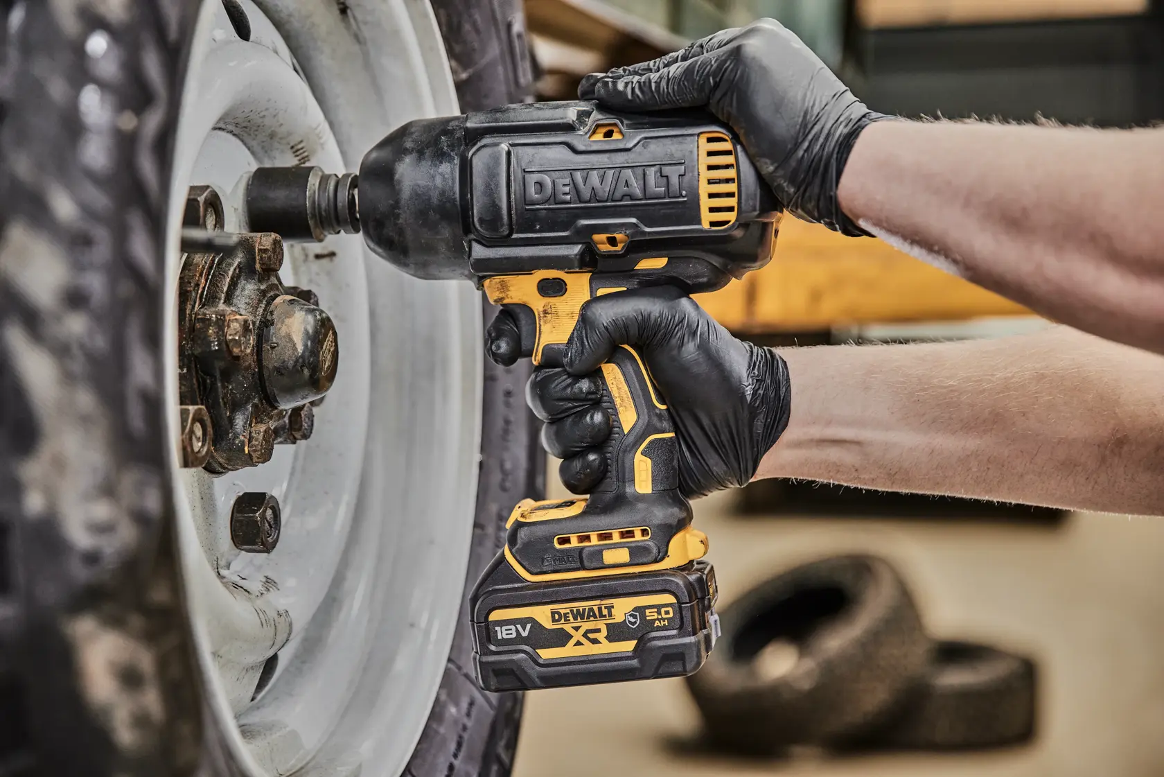 DEWALT cordless impact wrench loosening wheel nuts on a vehicle, used by a gloved hand.