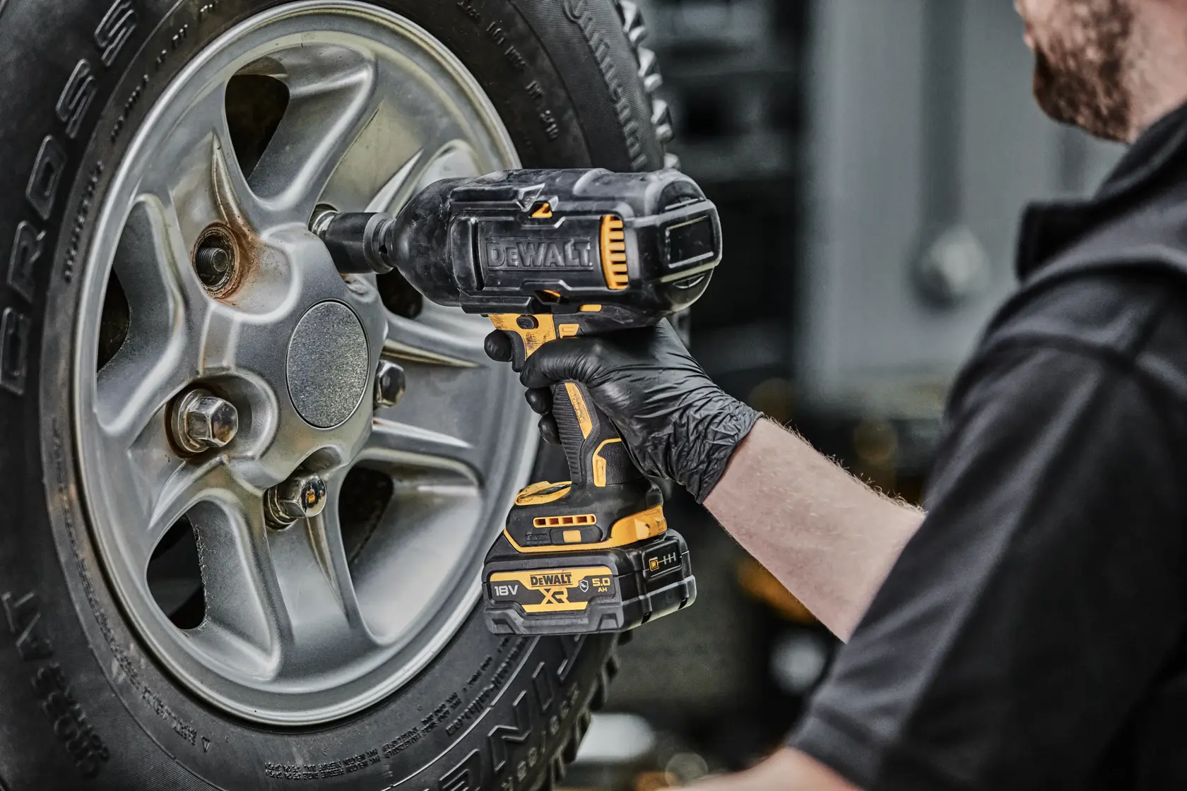 Person uses a DEWALT cordless impact wrench to tighten a lug nut on a car wheel.