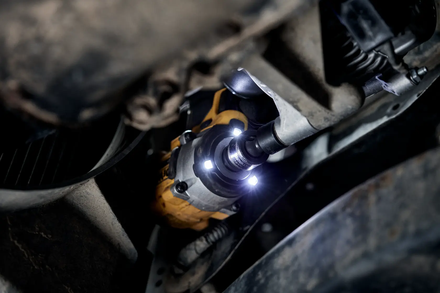 Close-up of a DEWALT cordless impact wrench being used to work on a vehicle's undercarriage, with built-in LED lights illuminating the workspace.