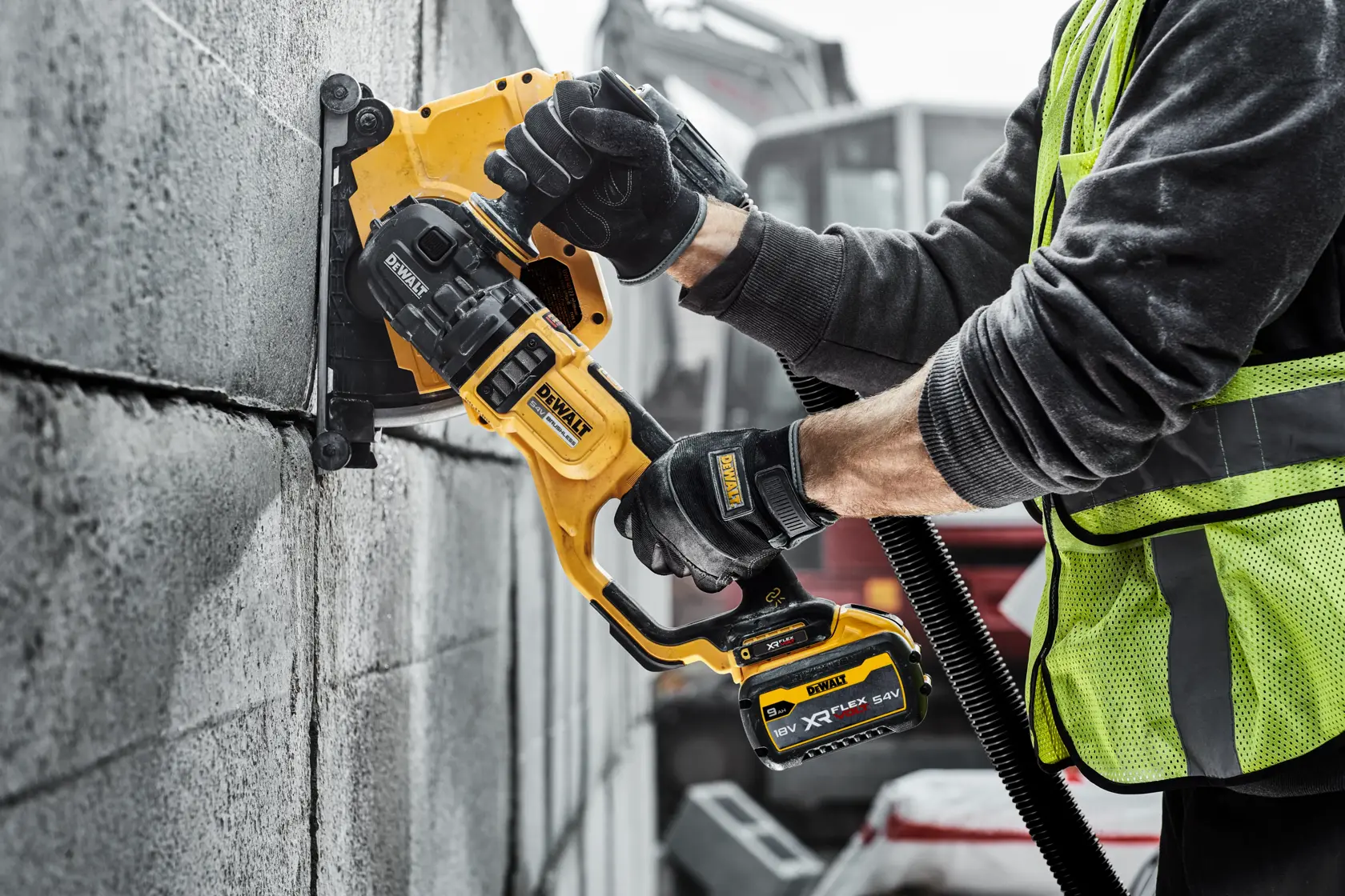 Worker using a DEWALT cordless wall chaser to cut grooves in a concrete block wall on a construction site.