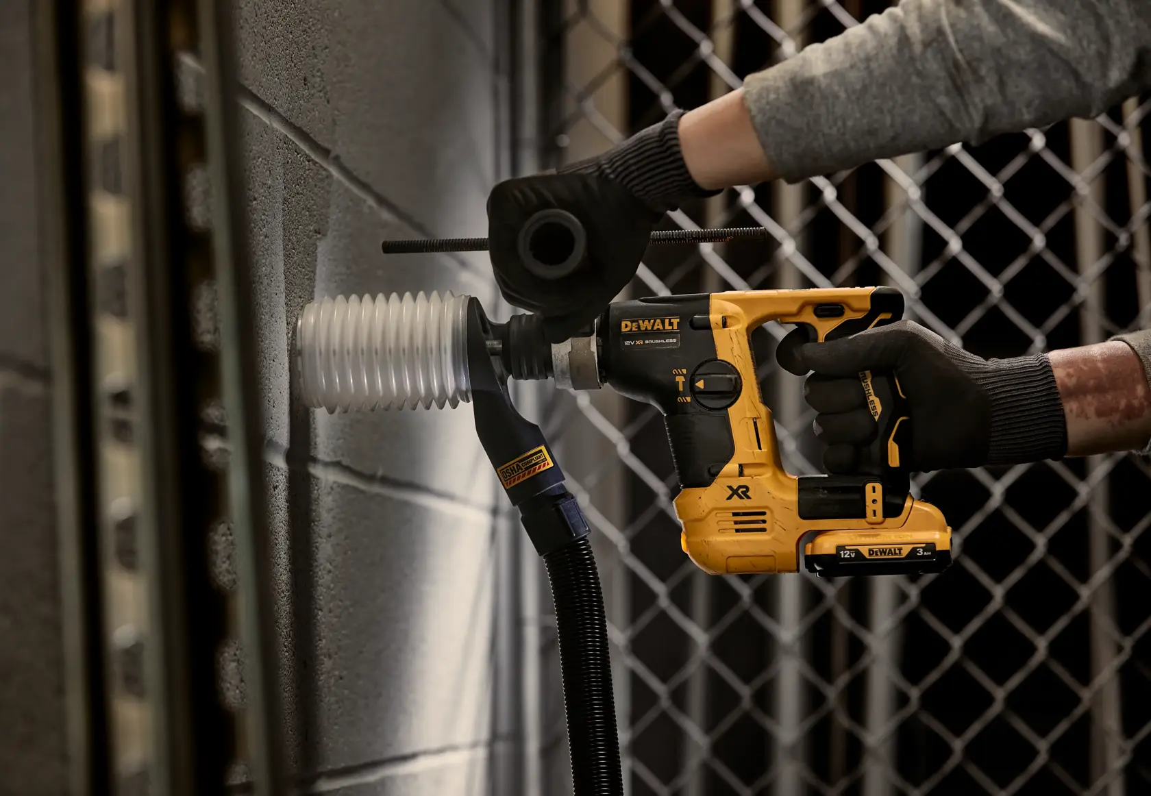 DEWALT cordless rotary hammer drilling into a concrete wall, equipped with a dust extraction attachment.