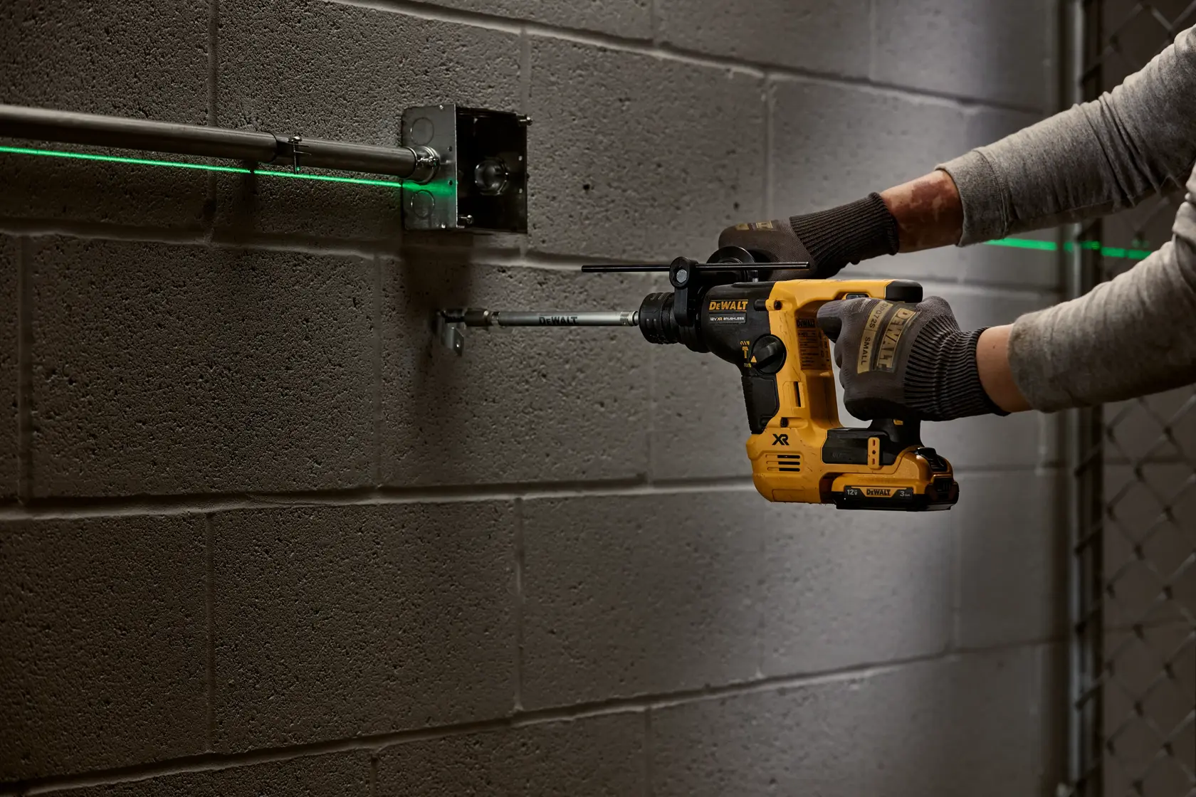 Person using a DEWALT rotary hammer drill on a concrete wall next to electrical conduit.