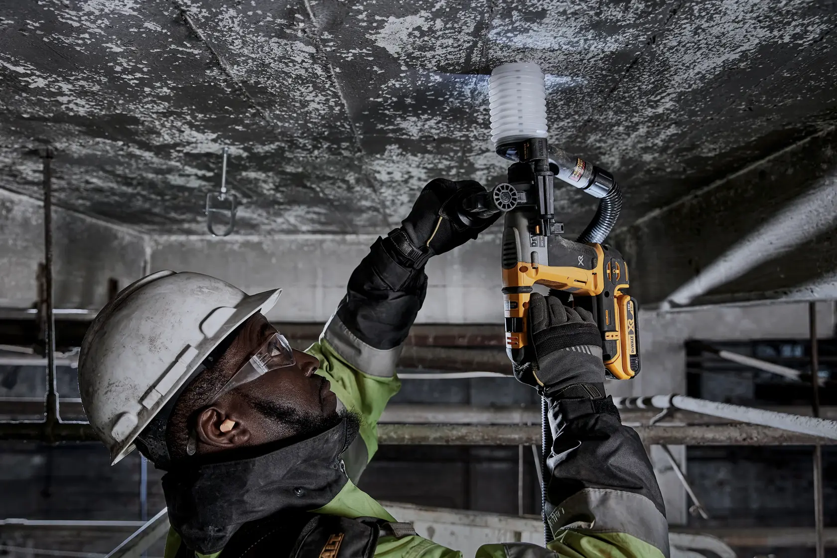 Worker uses DEWALT DCH172NT-XJ, DCH172NT on ceiling. Industrial setting, safety gear worn.