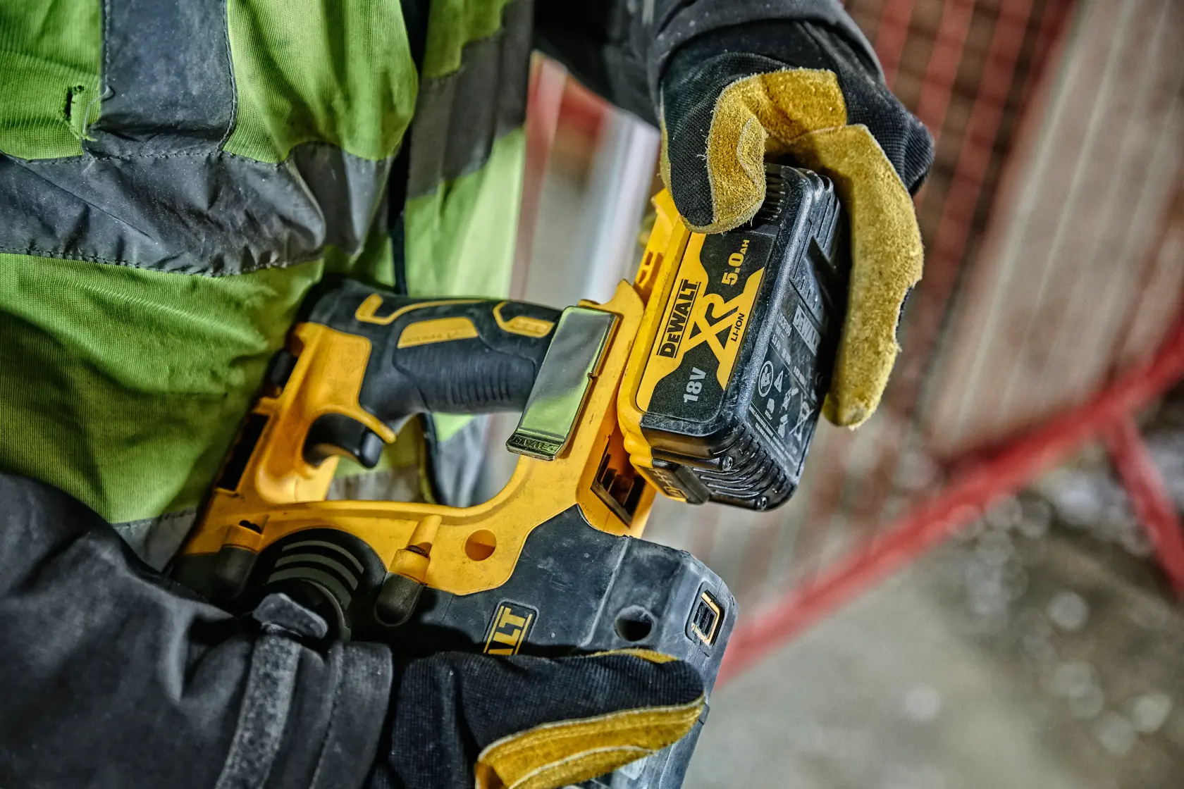 Gloved hand holds a DEWALT DCH274P2T cordless tool with 18V XR battery in a construction setting.