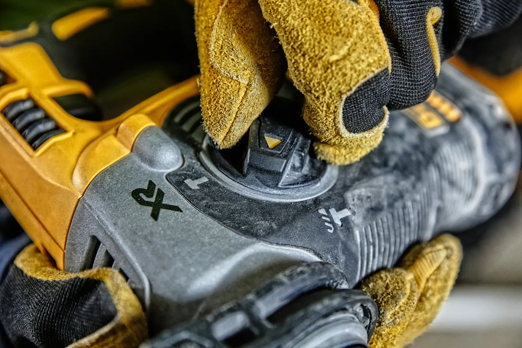 Gloved hand adjusting control on a yellow DEWALT power tool with visible function icons.