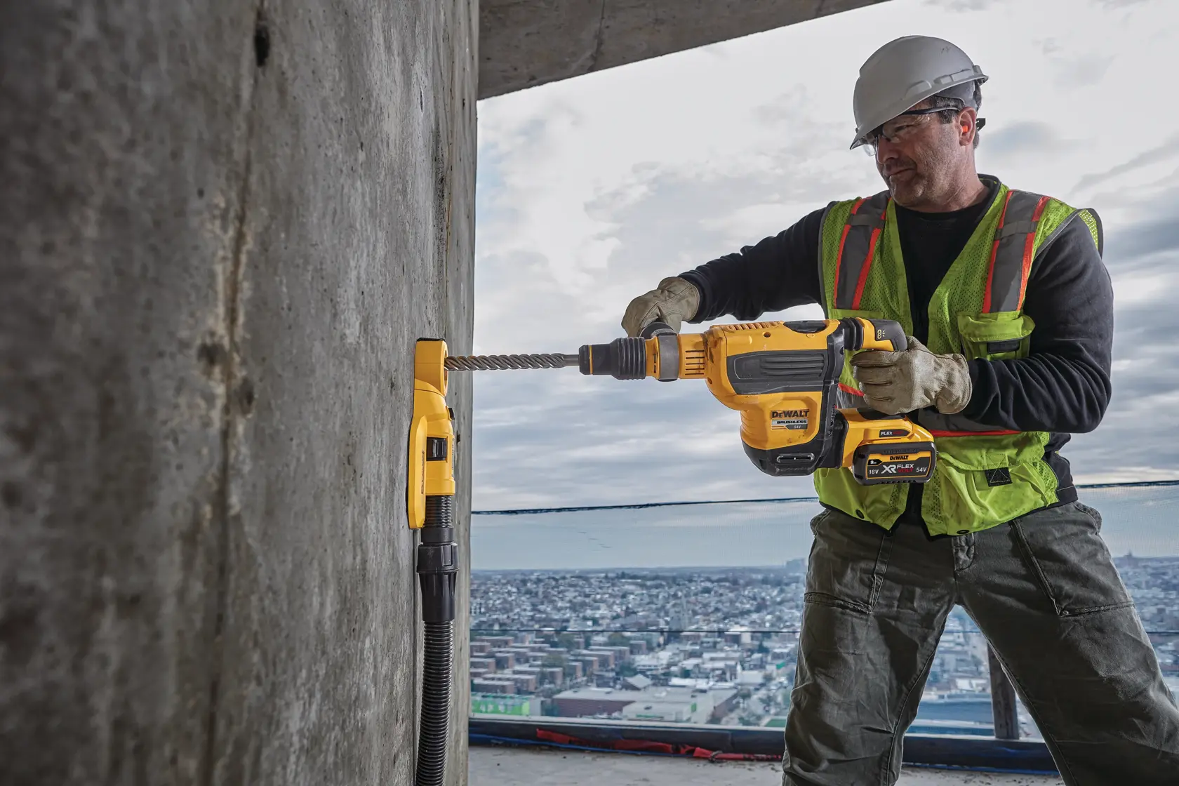 Worker uses DEWALT cordless rotary hammer drill on concrete wall at construction site.
