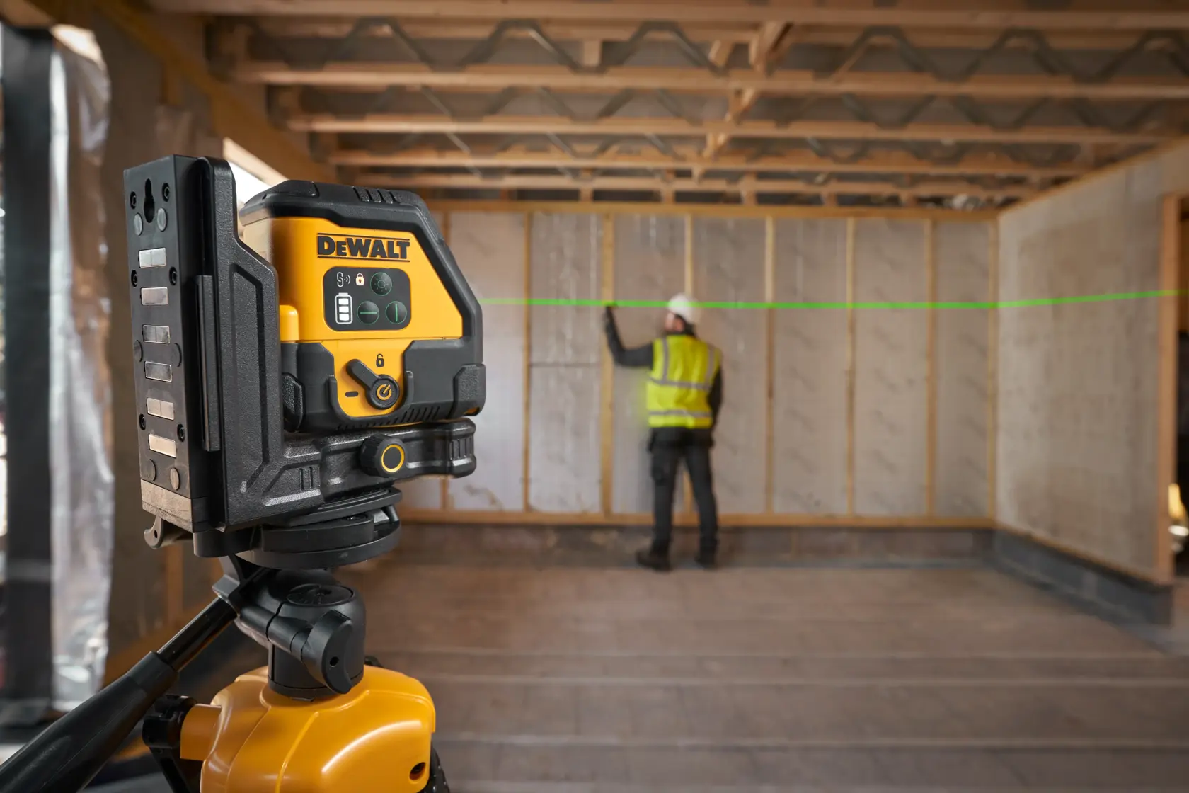 DEWALT laser level on tripod projects green line in construction room with worker marking wall.