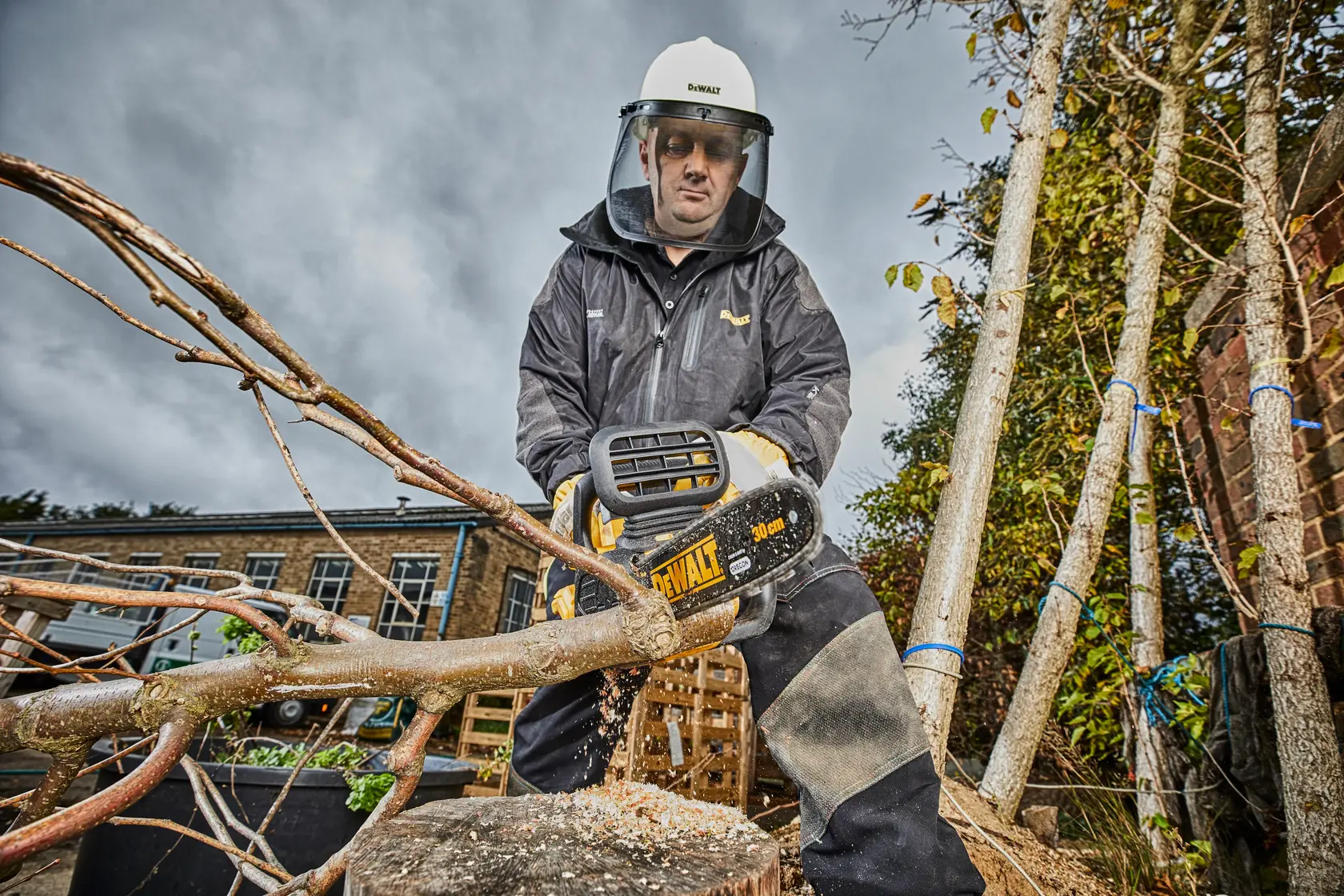 Person using DEWALT DCM565 chainsaw to cut tree branches outdoors, wearing safety gear.