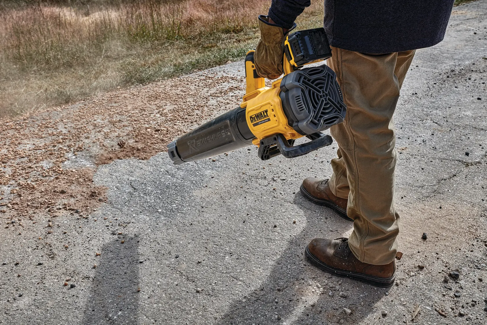 Person uses a DEWALT cordless blower to clear debris from a paved outdoor surface.
