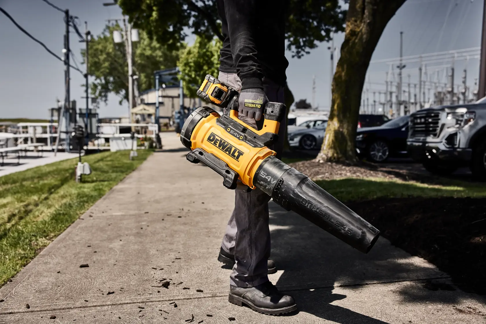 Person using a yellow DEWALT cordless leaf blower outdoors on a sidewalk.