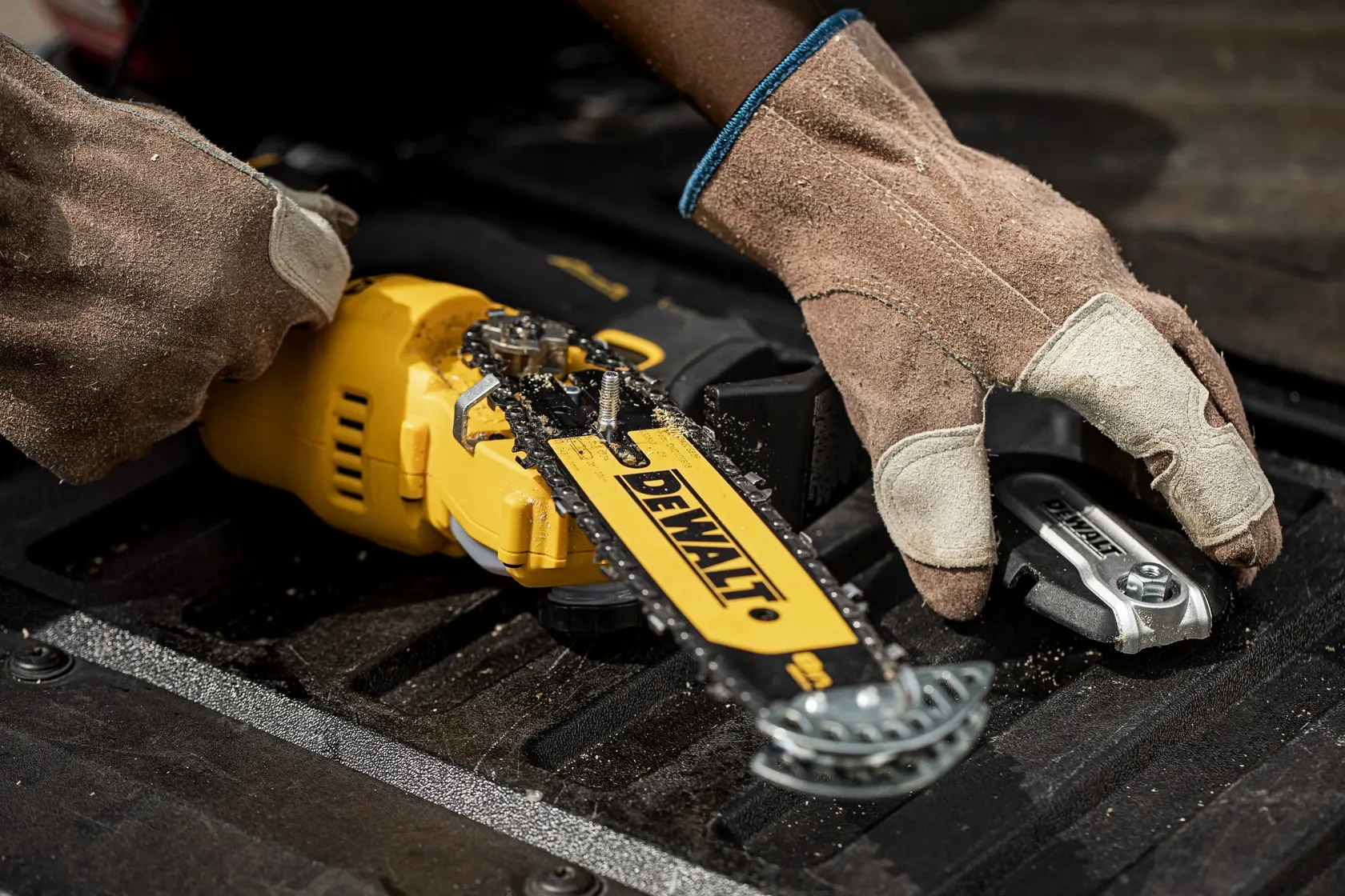 Worker with gloves assembling or inspecting a yellow DEWALT chainsaw and tool on a black surface.