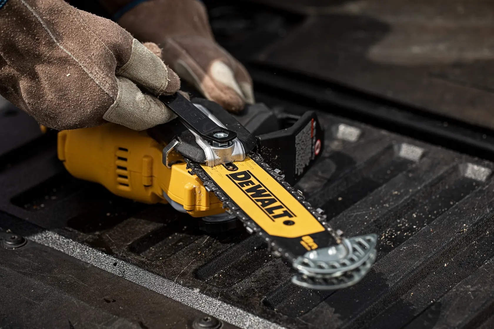 Gloved hands adjust a DEWALT chainsaw, model DCMPS520P1, lying on a dark textured surface.
