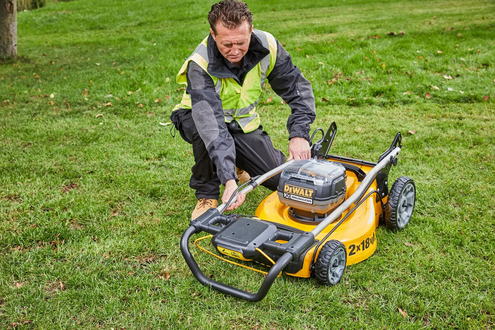 Person with safety vest adjusting DEWALT lawn mower DCMW564N on grass.