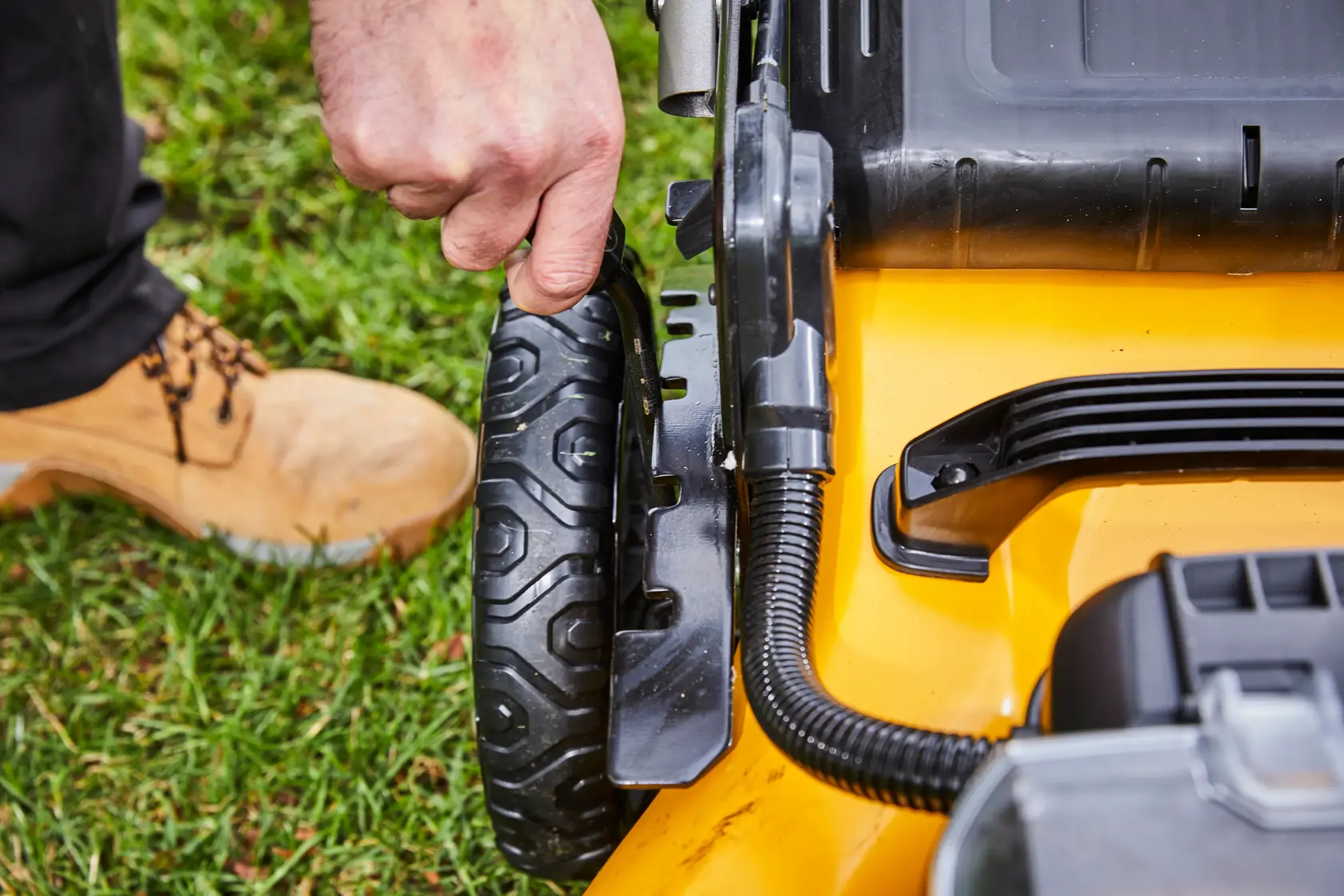 Hand adjusts the wheel height on a yellow DEWALT lawn mower outdoors.