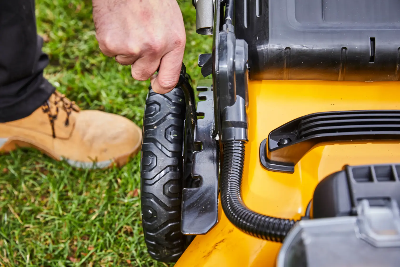 Hand adjusting the wheel height on a yellow DEWALT lawn mower, close-up view outdoors on grass.