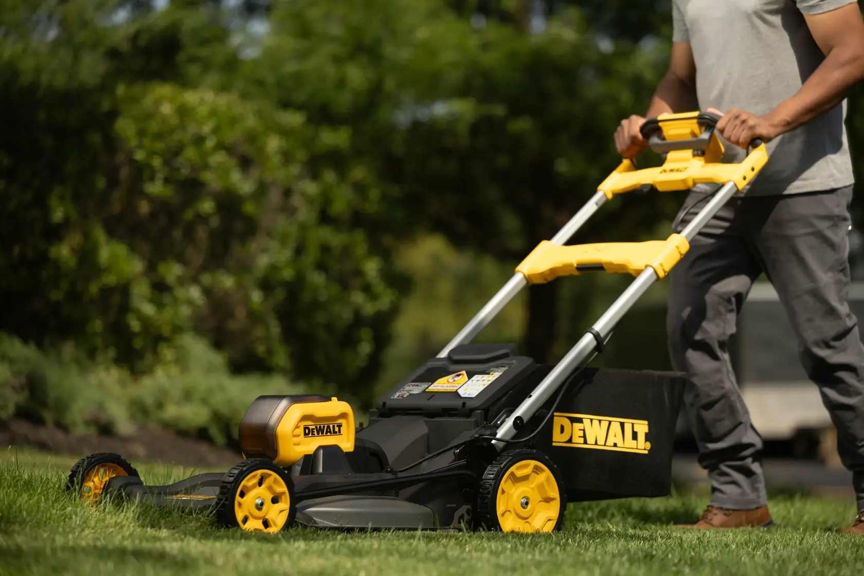 Person using a DEWALT cordless lawn mower on green grass outdoors, close-up view of mower and handle.