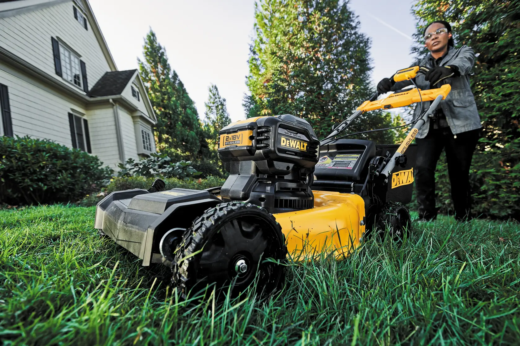 DEWALT lawn mower in use on grass near a house, user blurred for privacy.