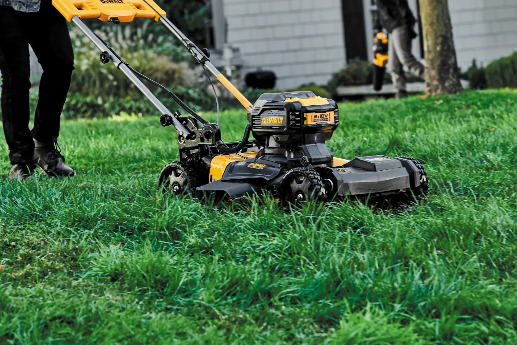 Yellow DEWALT lawn mower in use on green grass outdoors. Person partially visible pushing the mower.