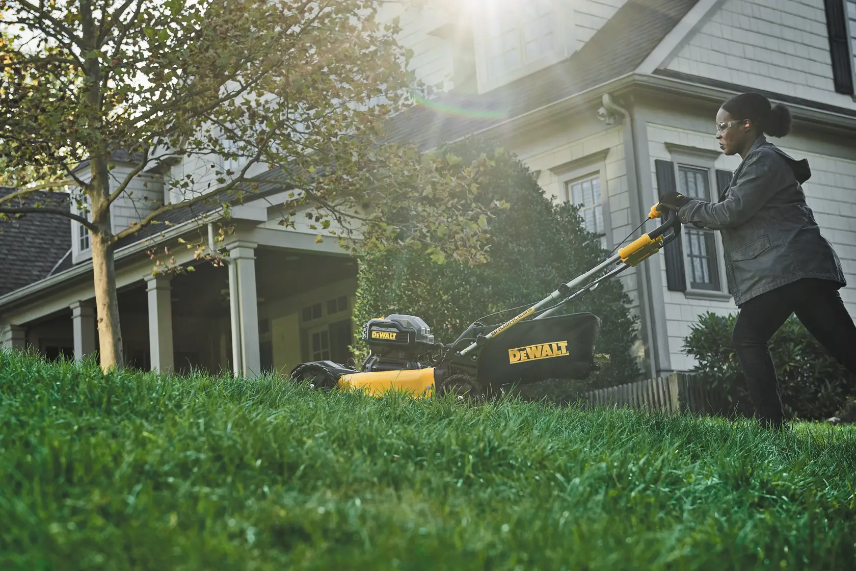 Person mowing lawn with a DEWALT cordless mower near a house on a sunny day.