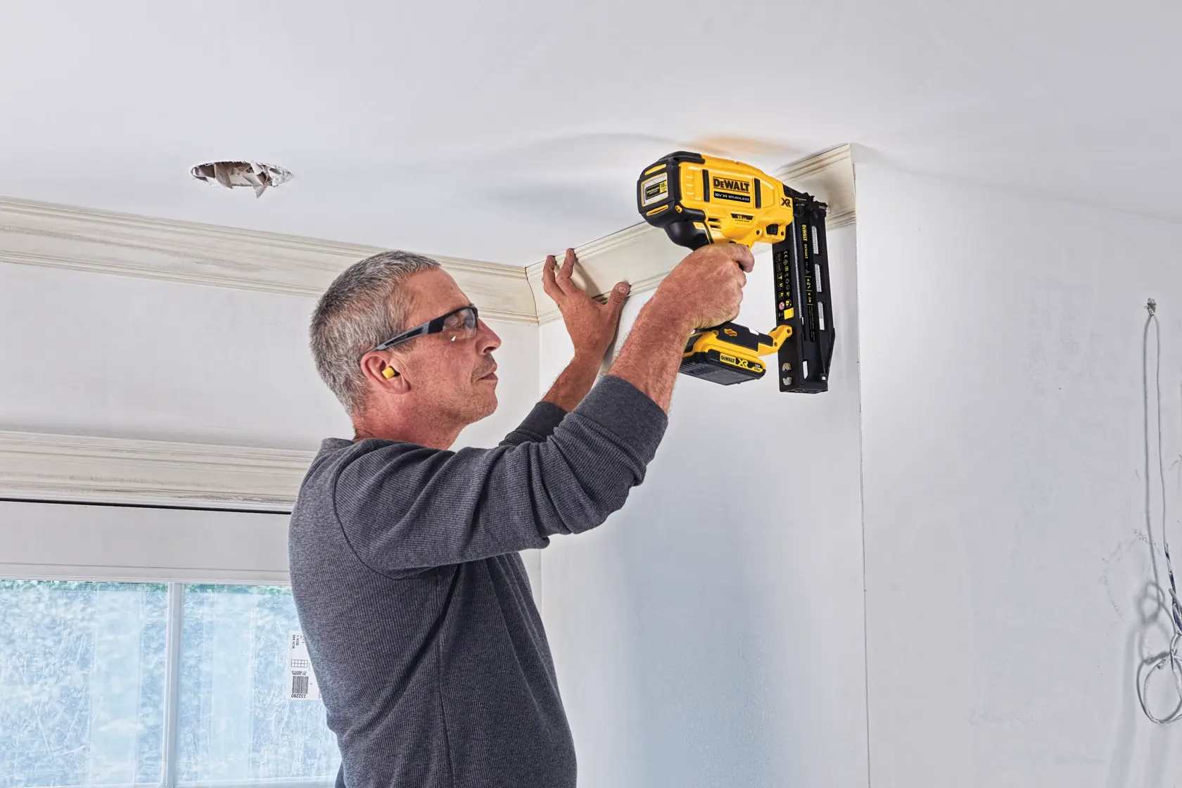 Person uses DEWALT nailer to install trim near ceiling in a bright room. Tool model: DCN662D2.