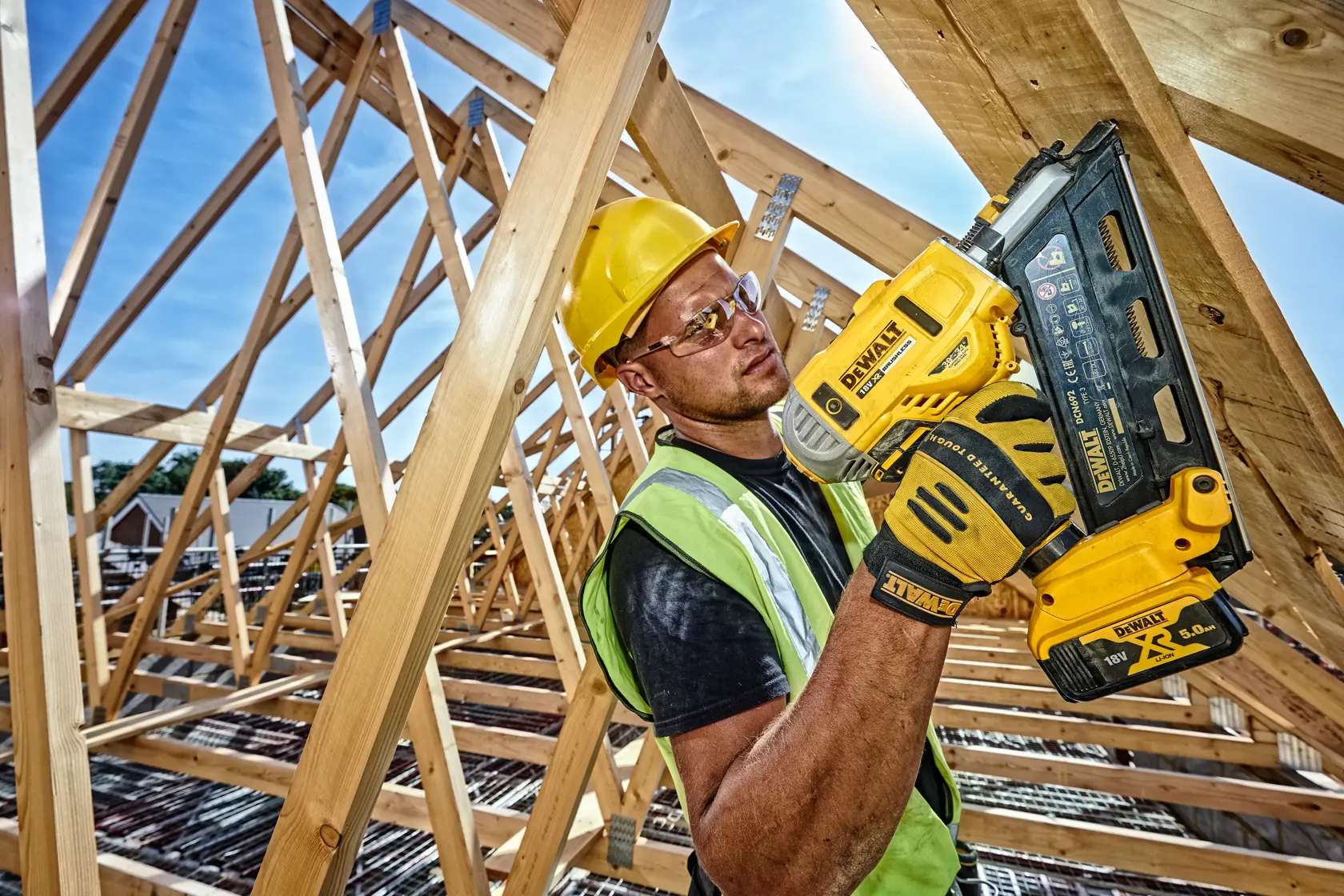 Worker uses DEWALT DCN692N nailer on wooden beams at a construction site, wearing safety gear and gloves.