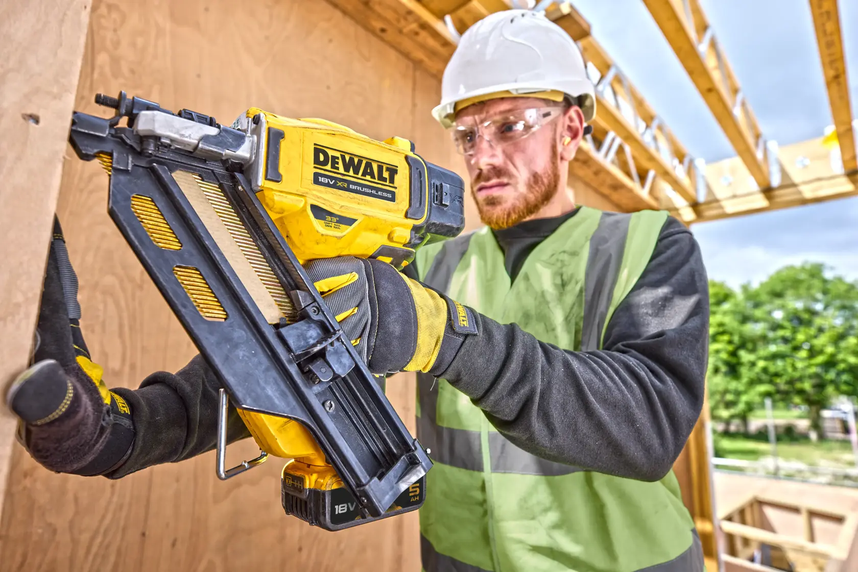 DEWALT DCN930P2 nailer held by a worker in safety gear on a construction site with wooden framing.