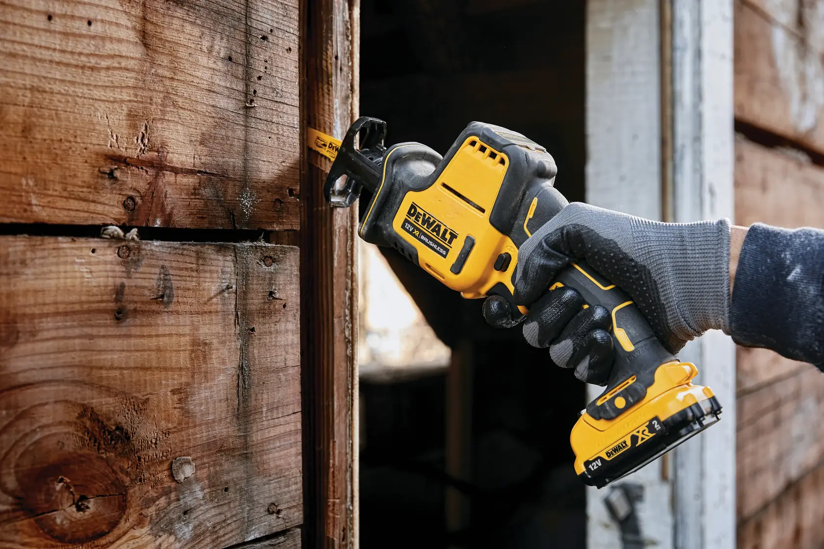 DEWALT cordless reciprocating saw cutting wood, held by a gloved hand near a wooden wall.