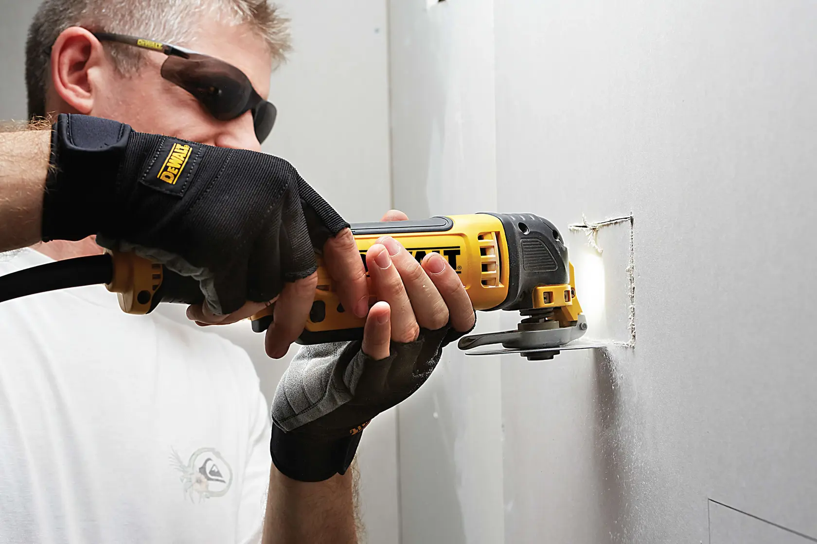 Person cuts drywall with yellow DEWALT DCS355D2 oscillating tool.